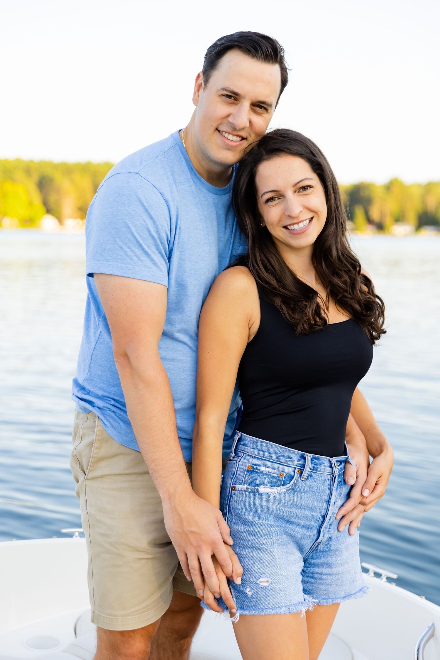 A couple stands together on a boat with a serene lake backdrop.