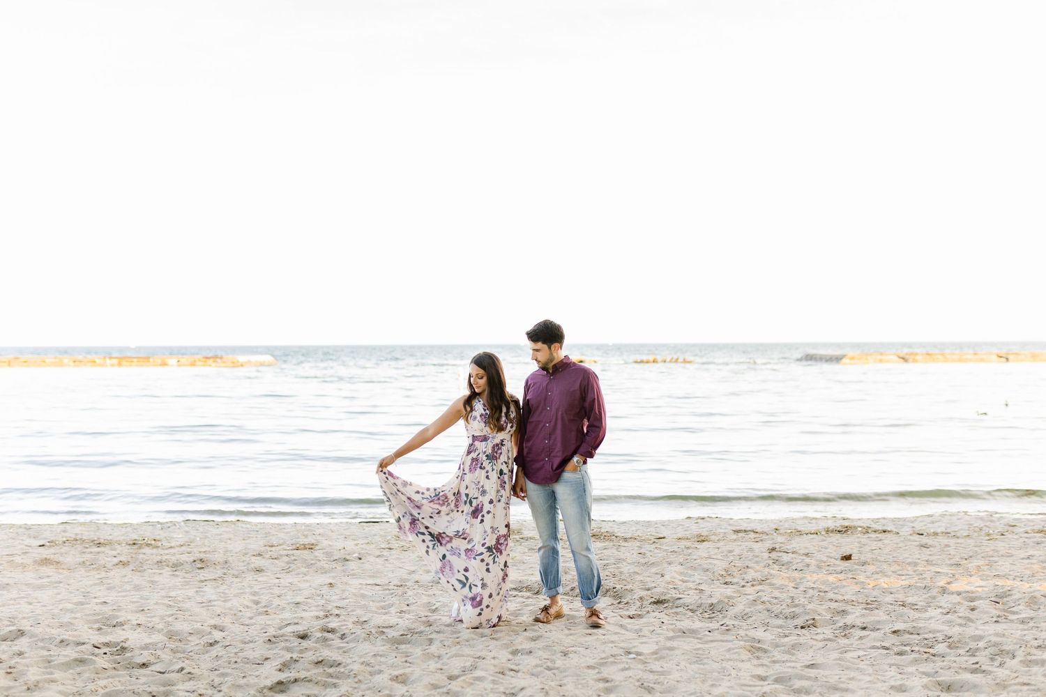 A couple walks along the shoreline at sunset wearing coordinated casual outfits.