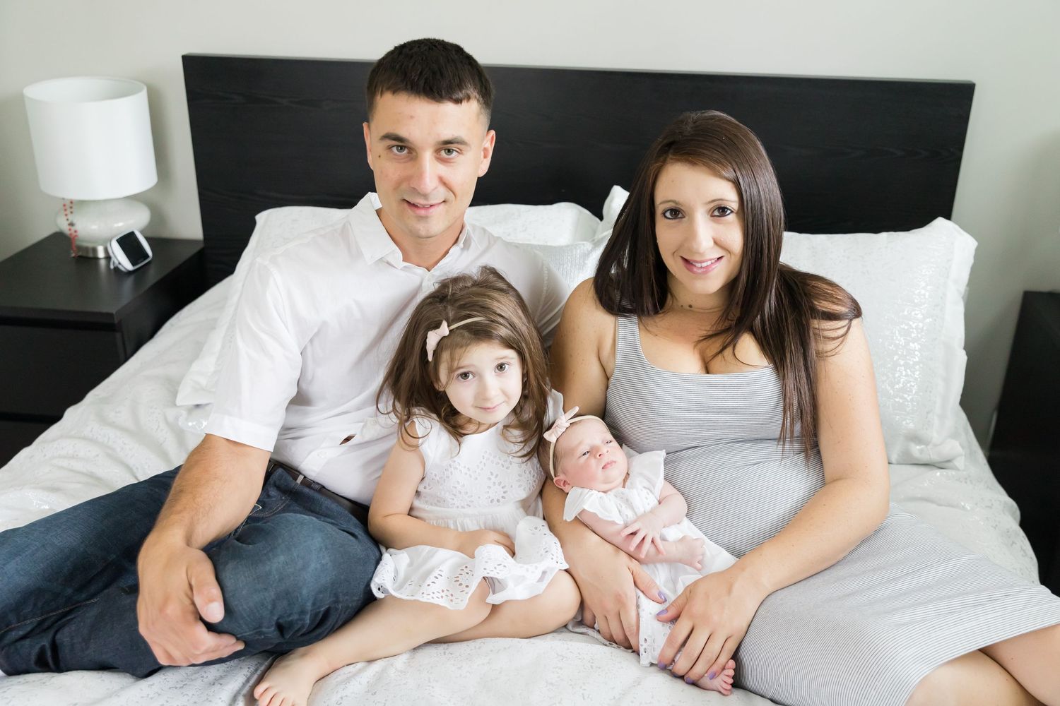 Family portrait on bed with white and gray color scheme.