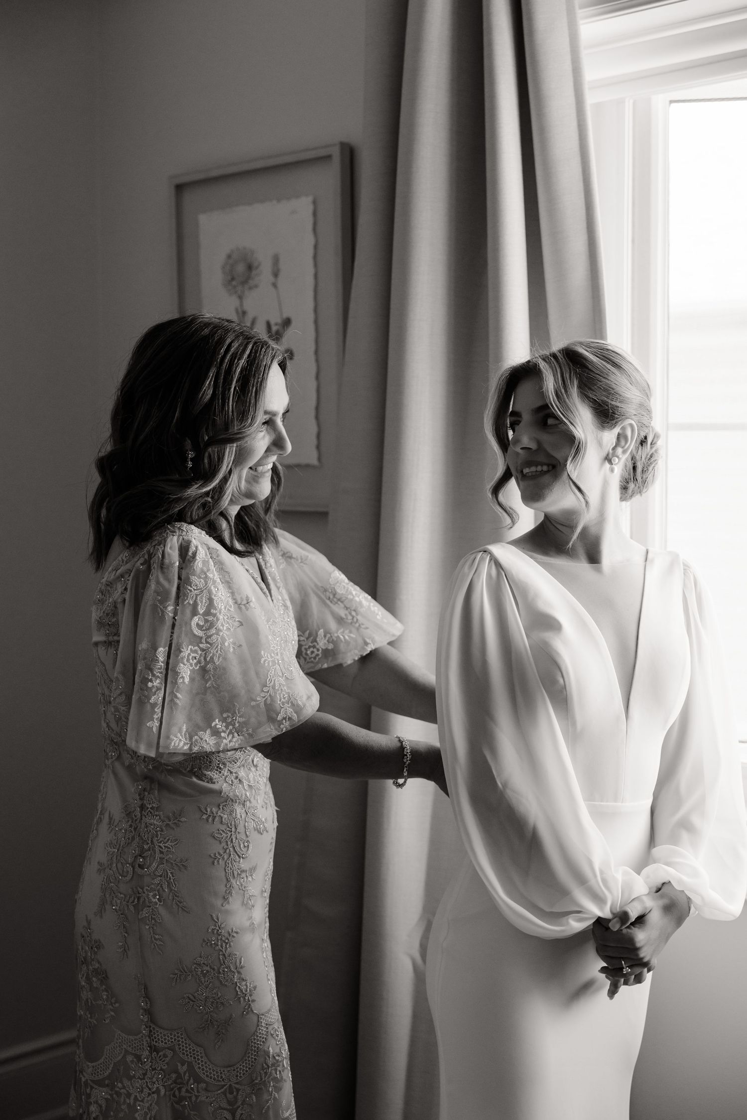 A black and white photo captures two people in elegant dresses sharing an intimate moment.