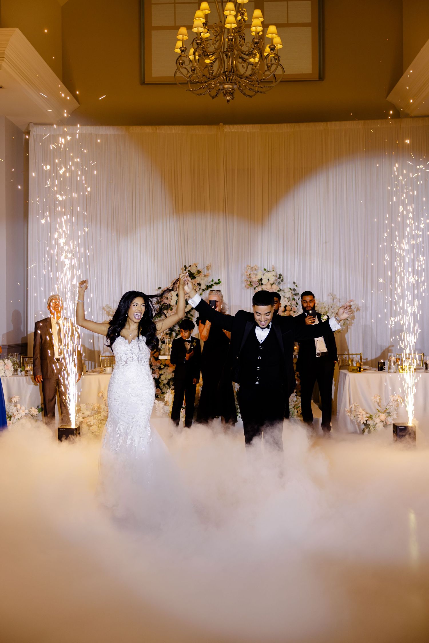 Wedding couple makes grand entrance through sparkling pyrotechnics and low-lying fog at reception venue.