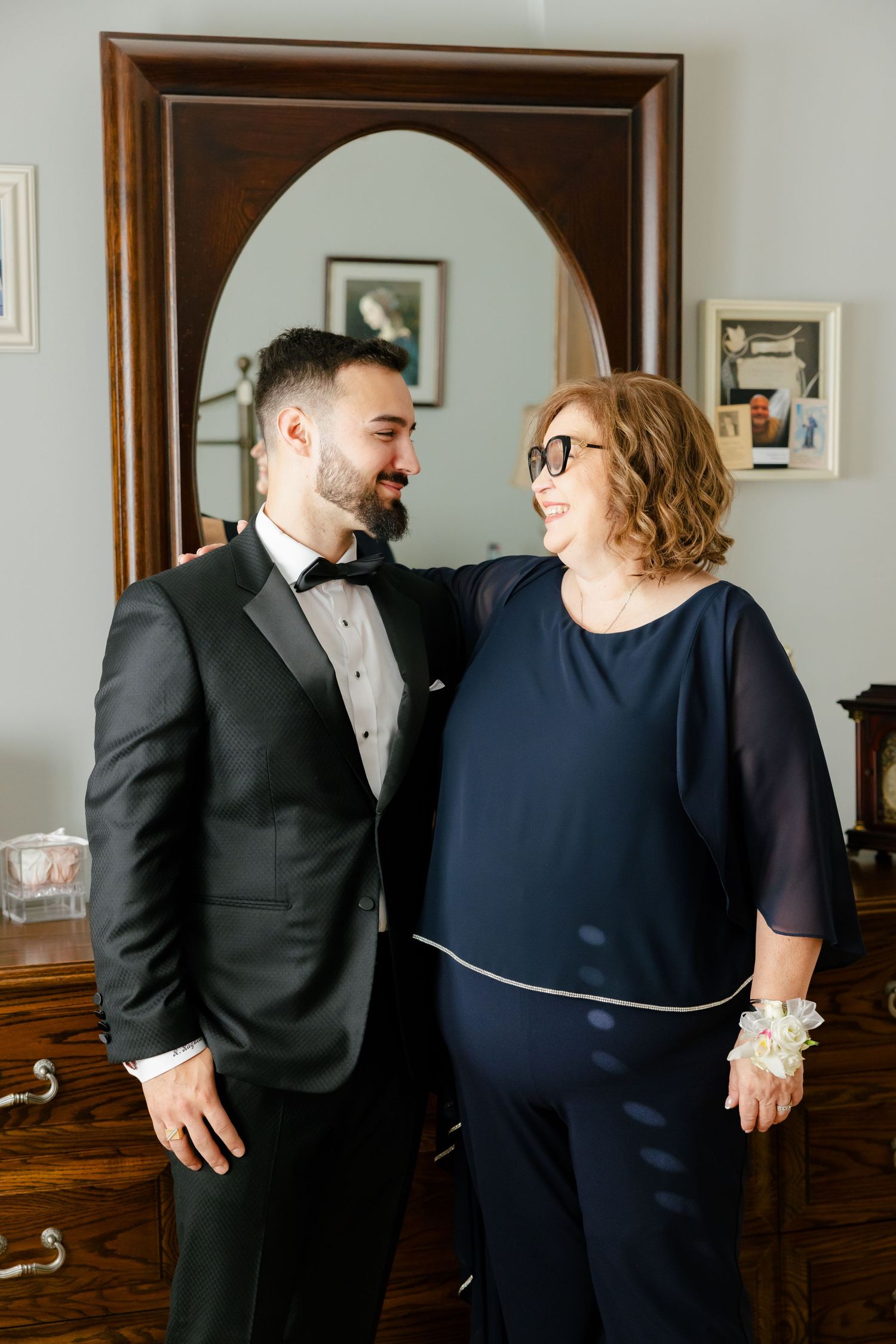 Heartwarming moment shared during formal occasion preparations beside wooden furniture.
