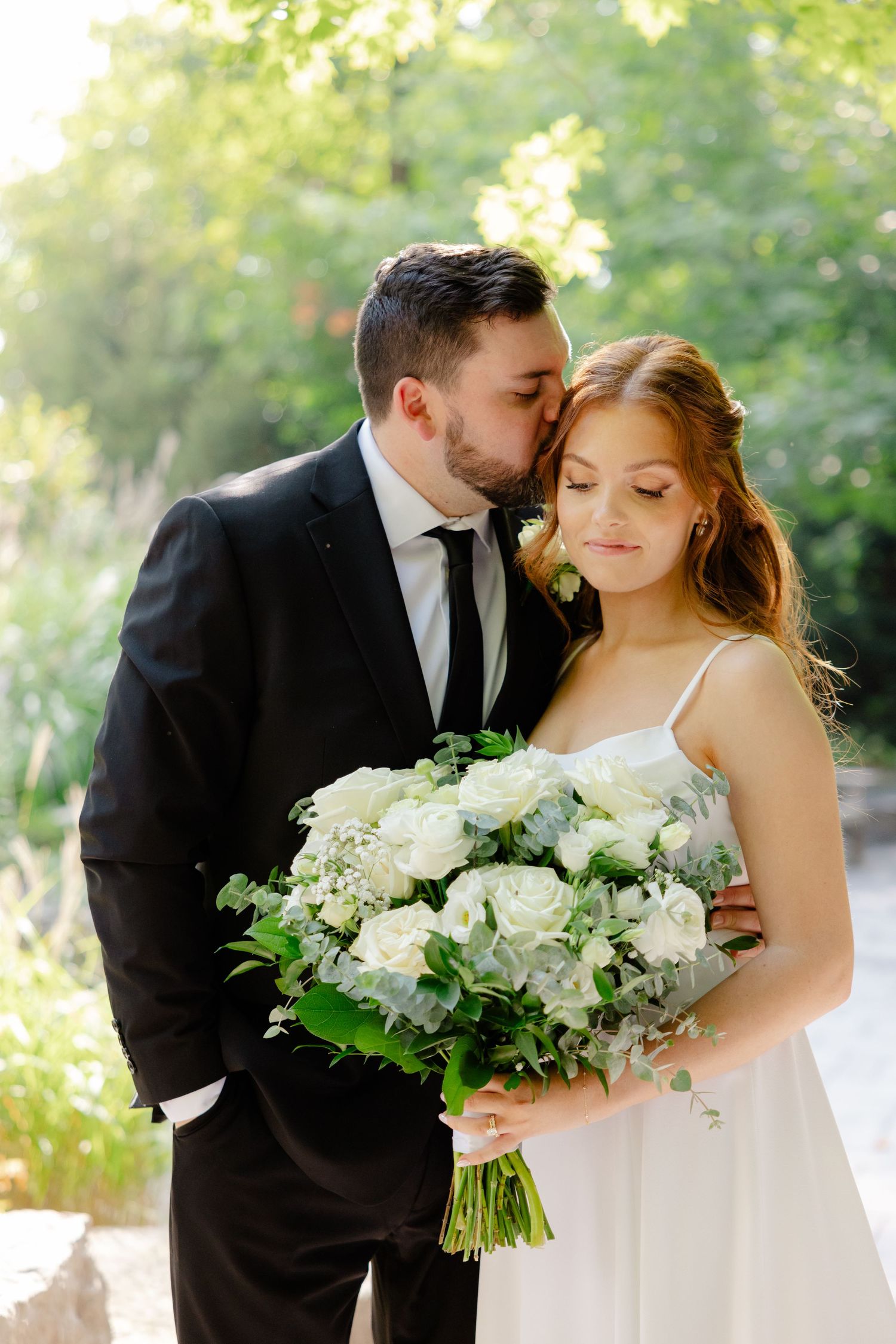 An intimate wedding moment captured in a sunlit garden with white floral arrangements.