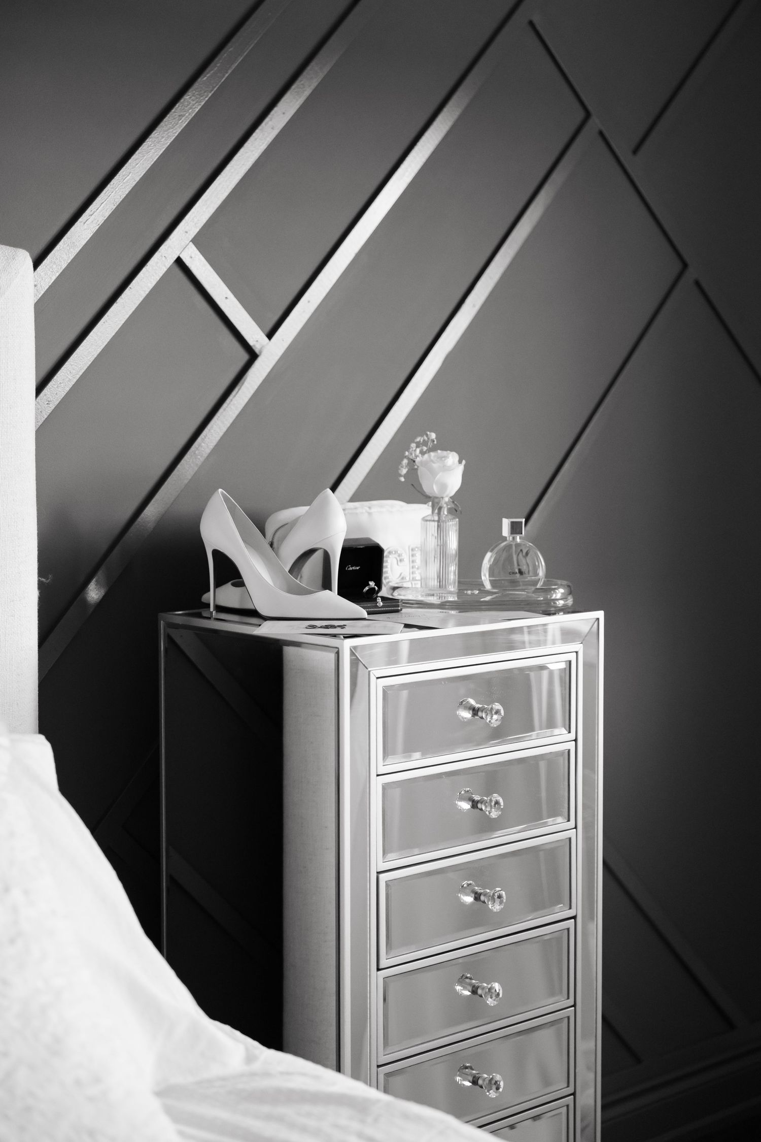 Wedding accessories including shoes and perfume bottles on a mirrored dresser against geometric wall.