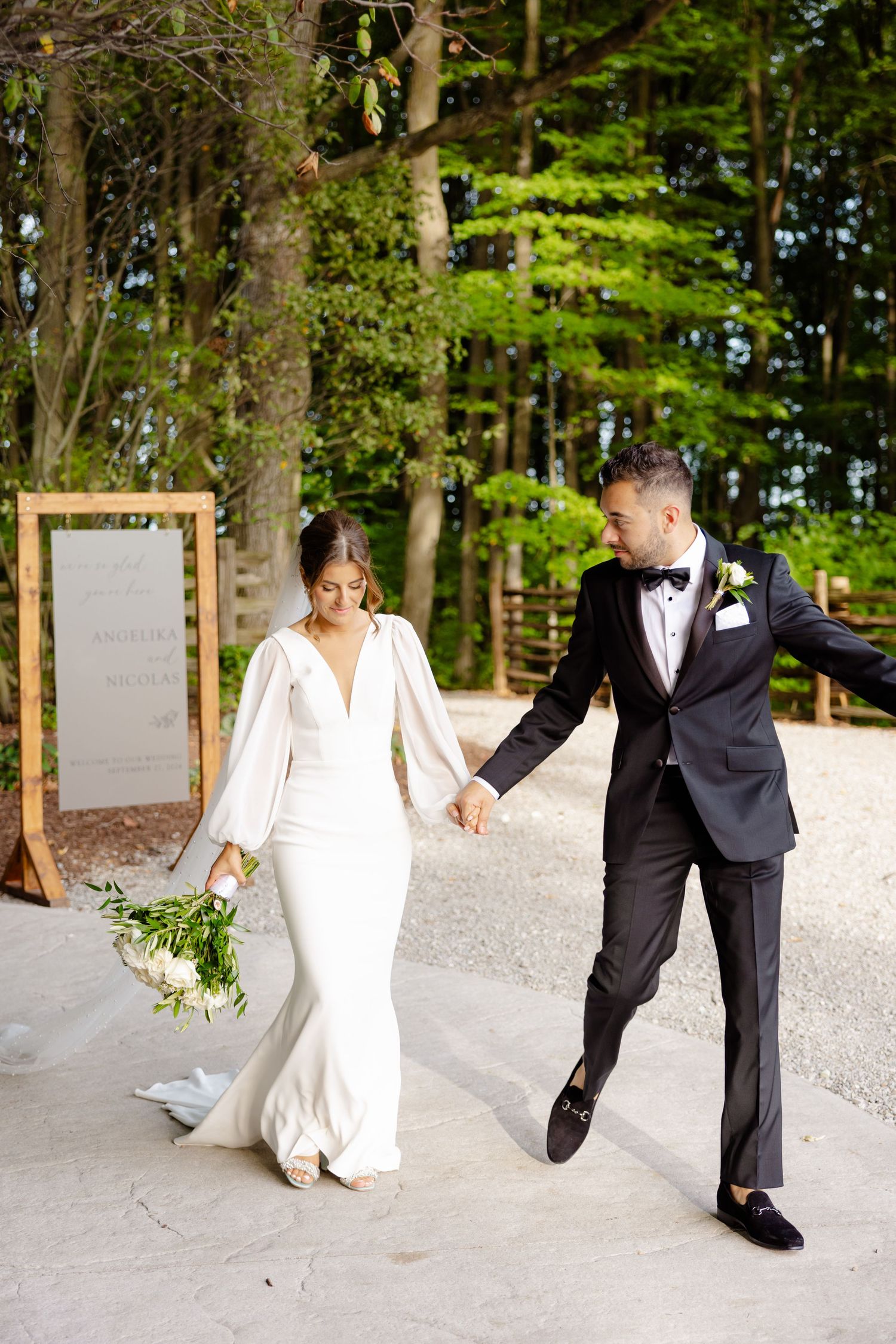 Happy newlyweds walking hand in hand along a forest path with a decorative mirror display.