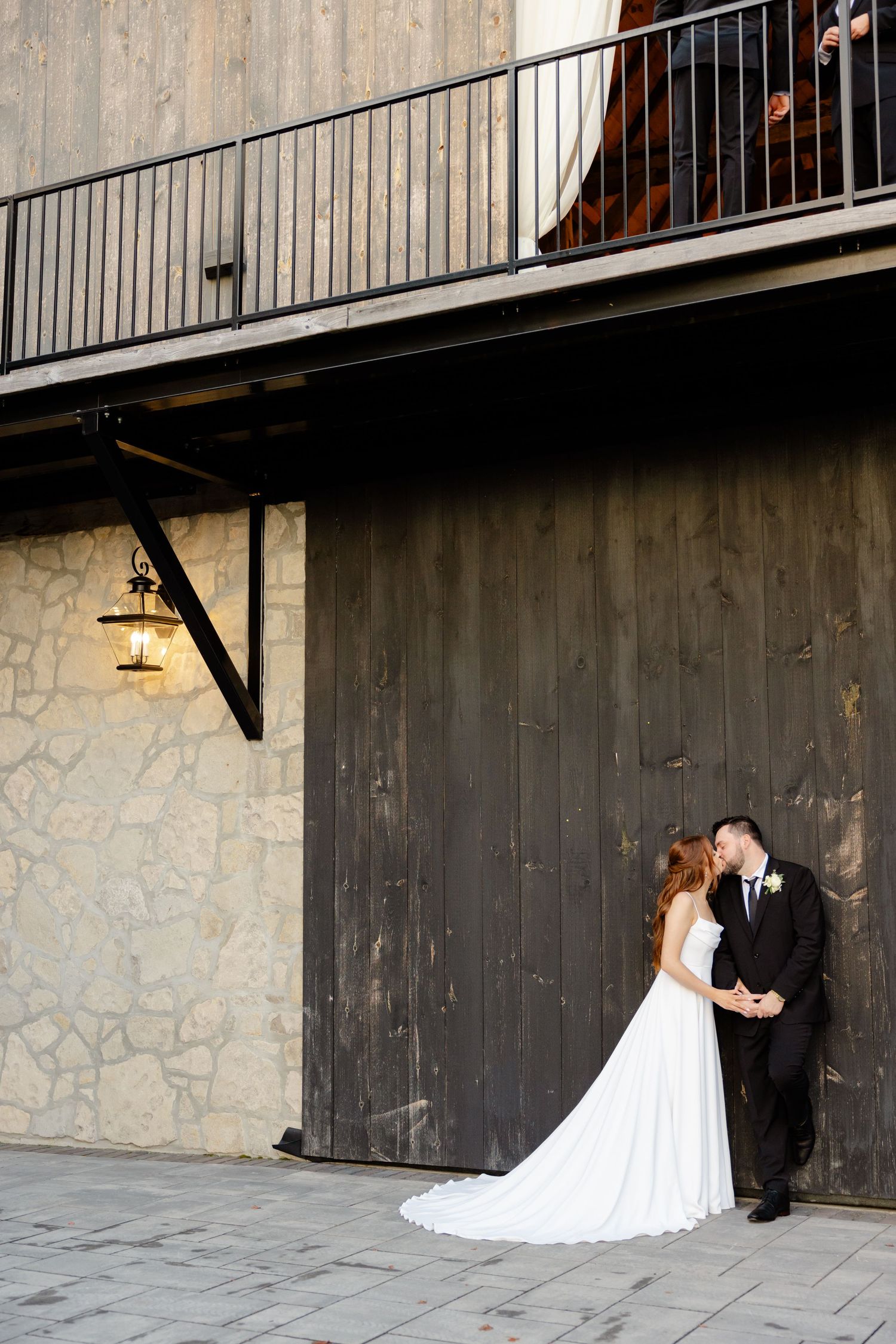 Elegant wedding photo beneath industrial-style balcony with rustic backdrop.