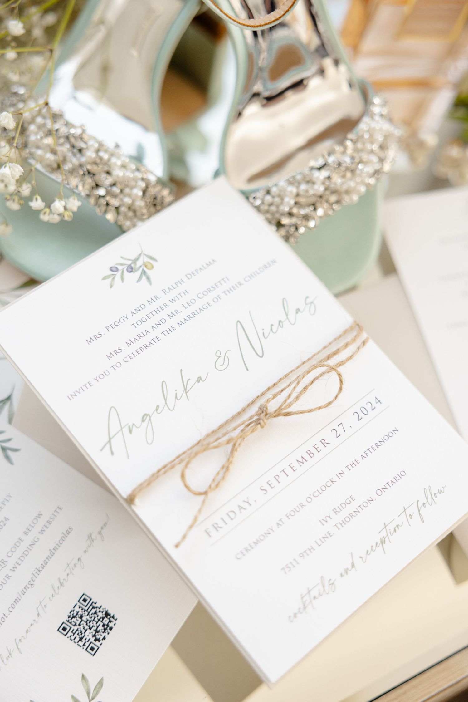 Elegant wedding invitation with twine bow and mint green accents displayed with decorative shoes.