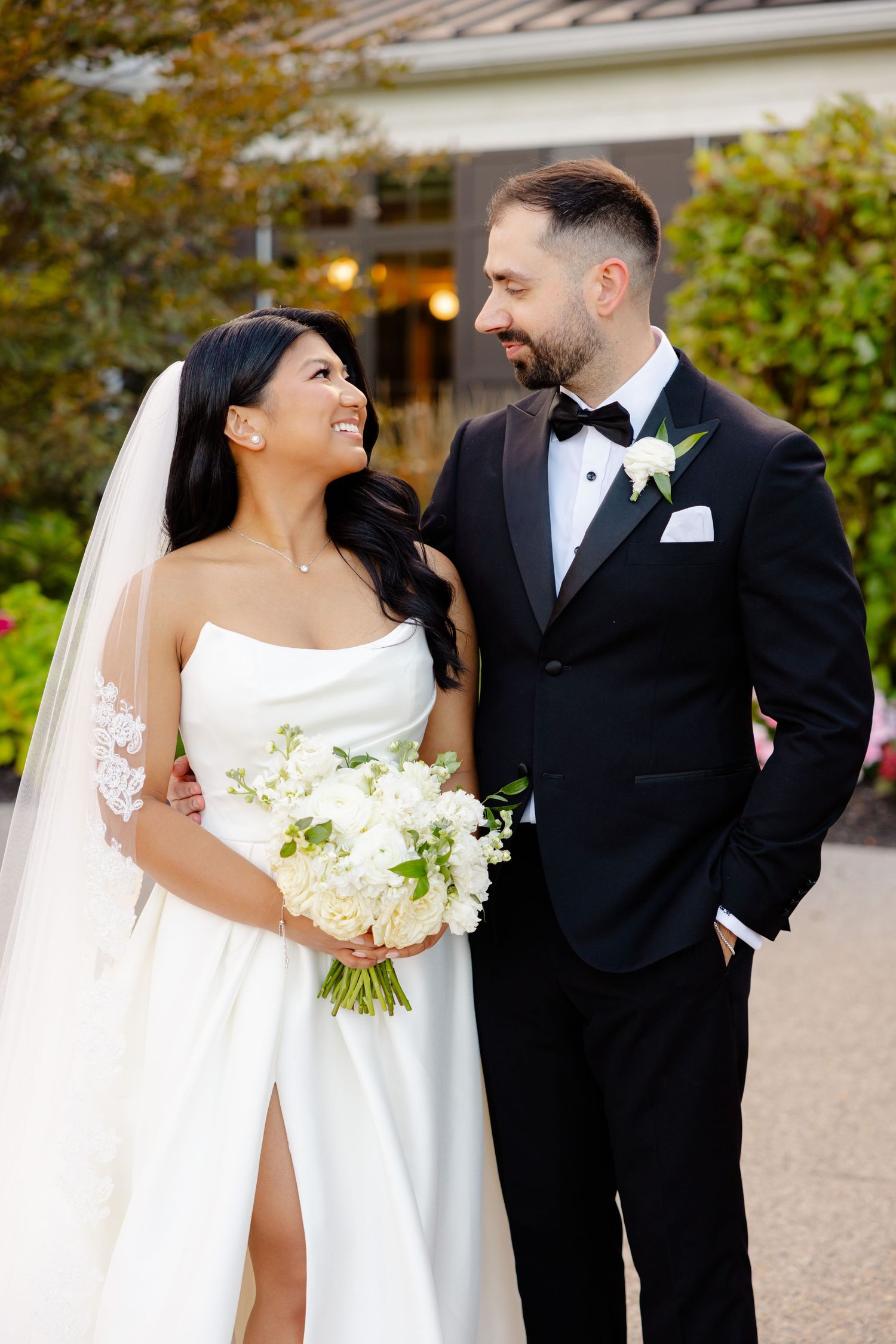 Happy newlyweds exchange loving glances while posing for portraits outdoors.