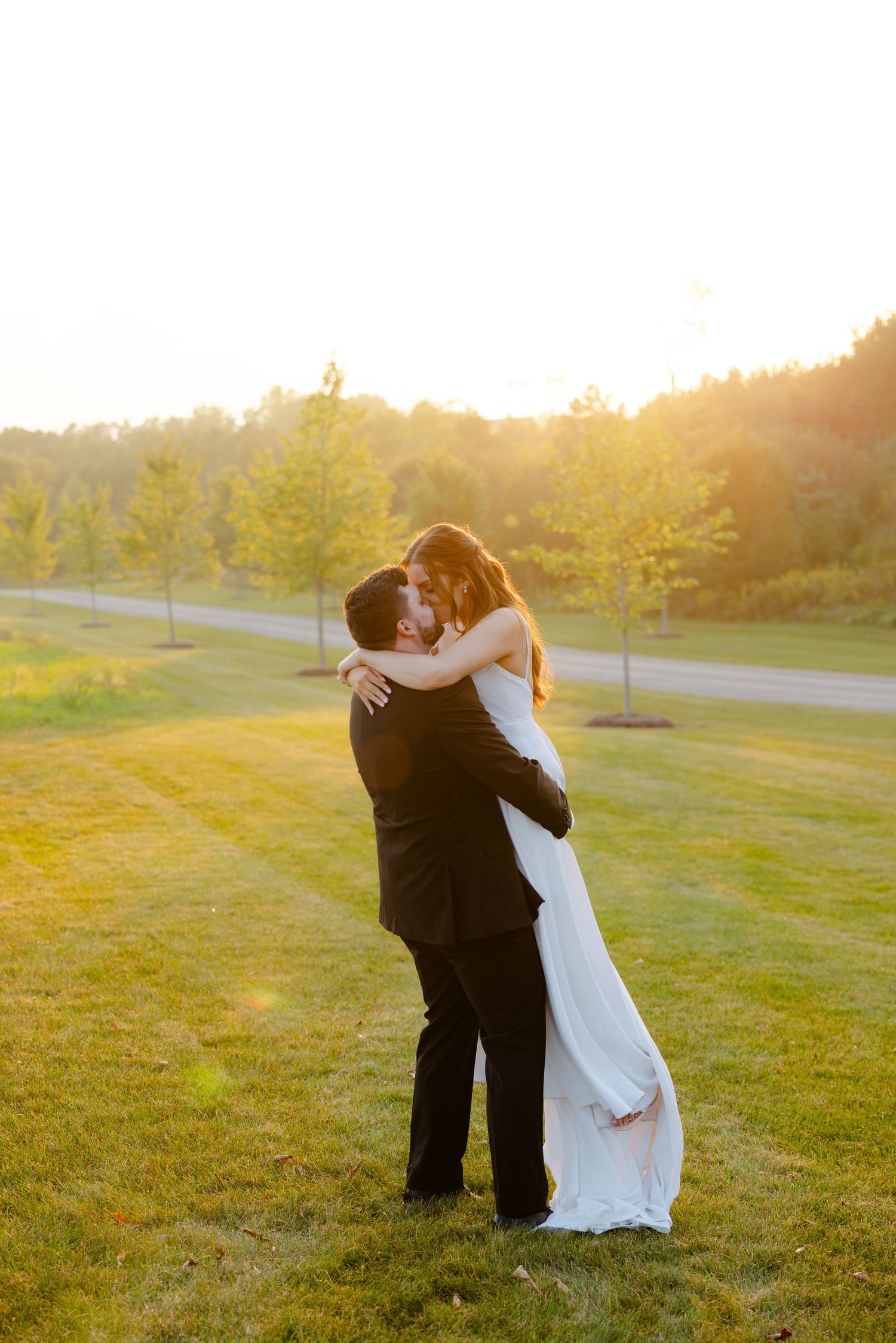 Bride and groom share a romantic dance pose outdoors with golden sunset lighting.