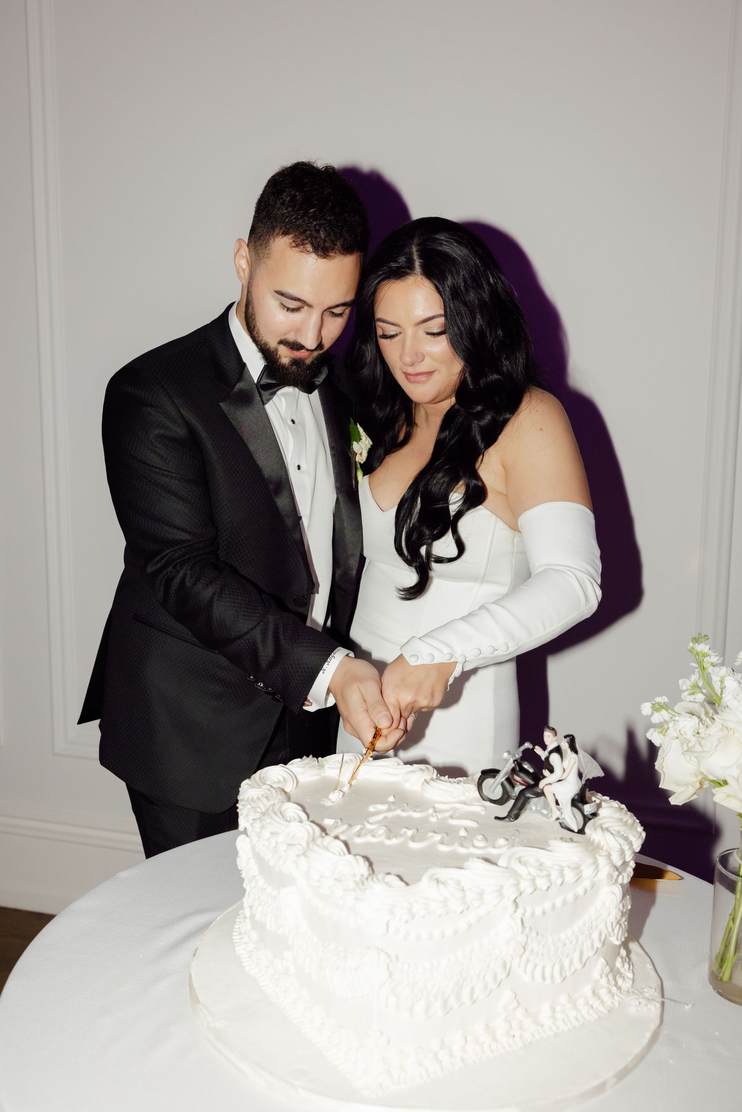 A couple shares an intimate moment while cutting their traditional white wedding cake.