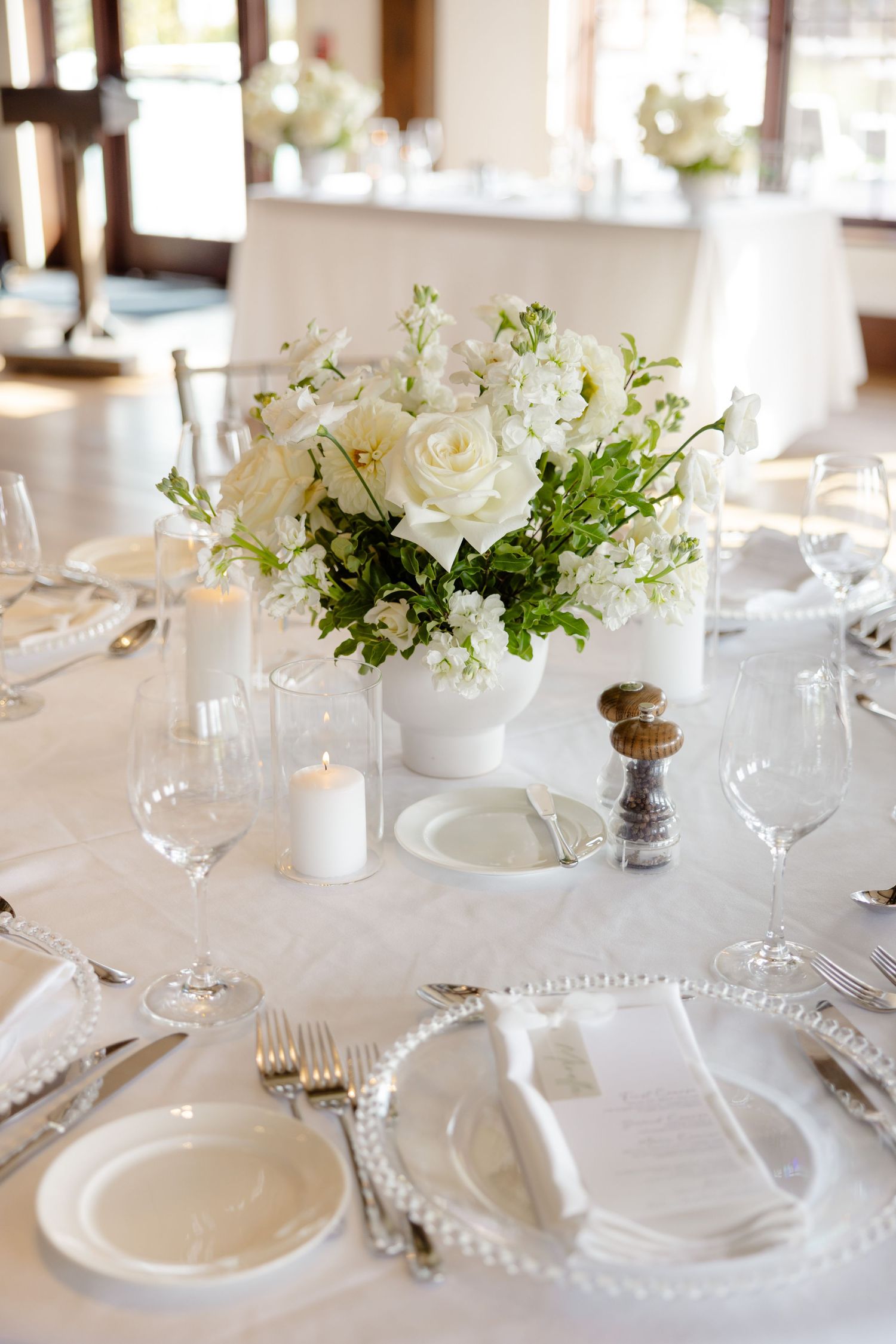 White floral centerpiece with roses and delicate greenery on an elegantly set round dining table.