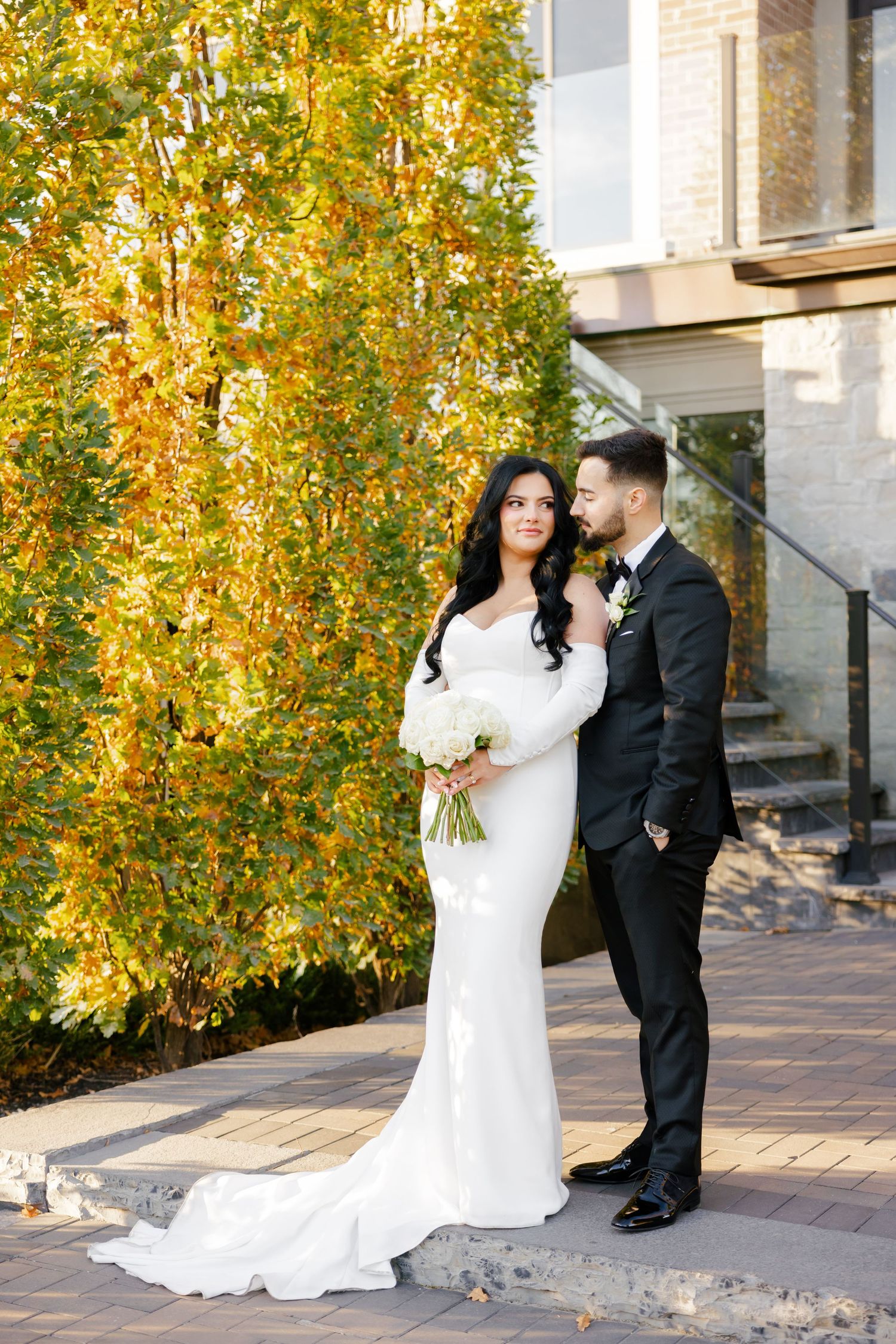 Elegant newlyweds share a moment by golden autumn trees with bride in flowing white gown with train.