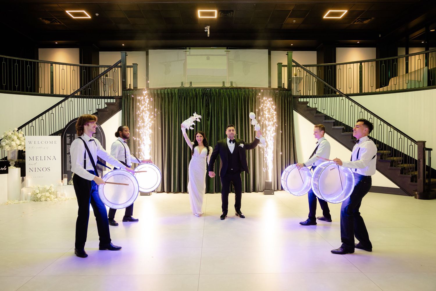 Wedding performance featuring drummers in formation on a white dance floor with twin staircases.