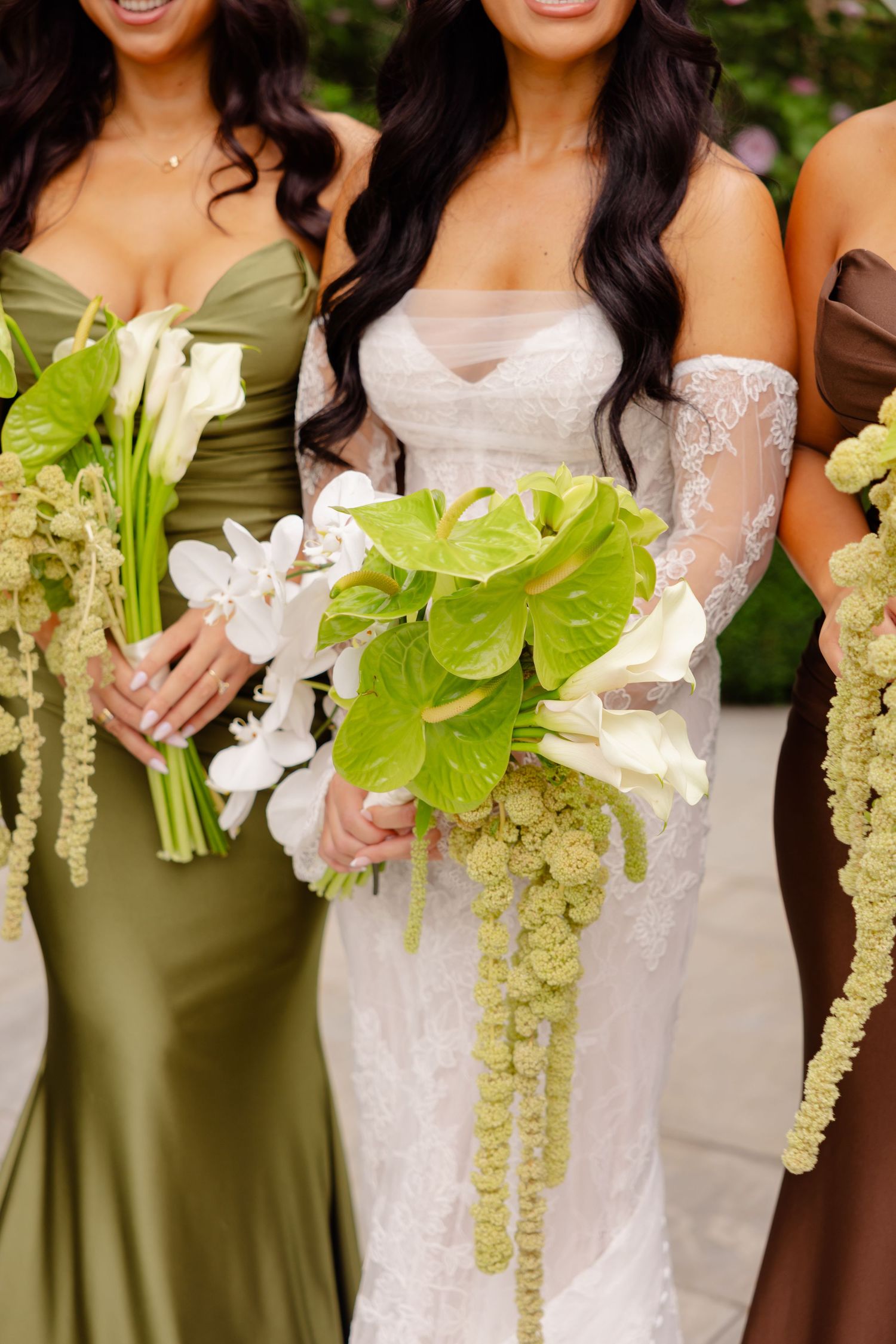 Bridesmaids in olive green dresses hold stunning tropical bouquets with white orchids and large green leaves.