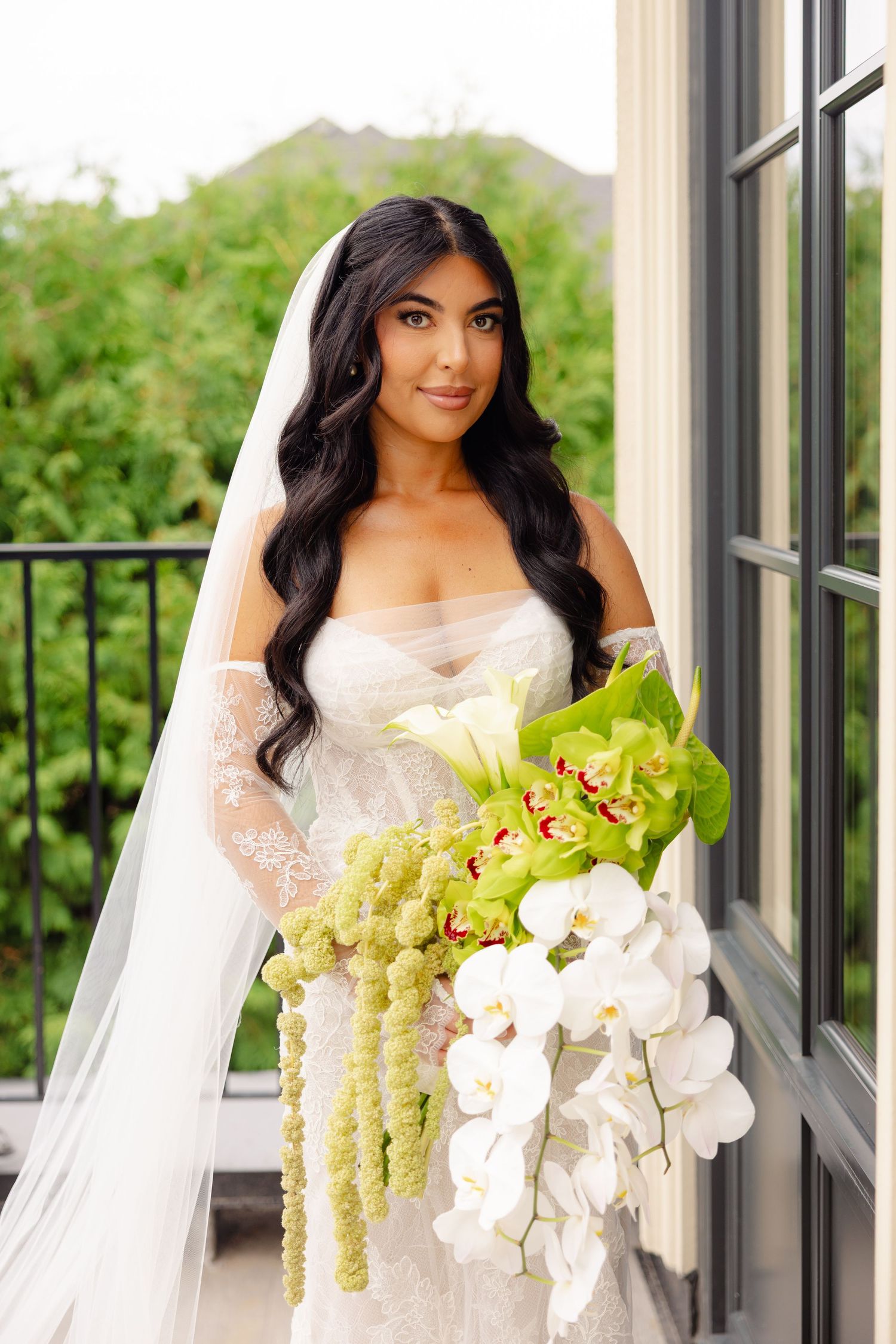 A bride holds an elegant bouquet featuring white orchids and green amaranthus in an indoor setting.