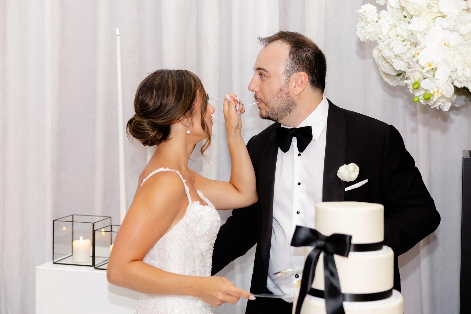A newlywed couple shares intimate moments in formal wedding attire against a white backdrop.