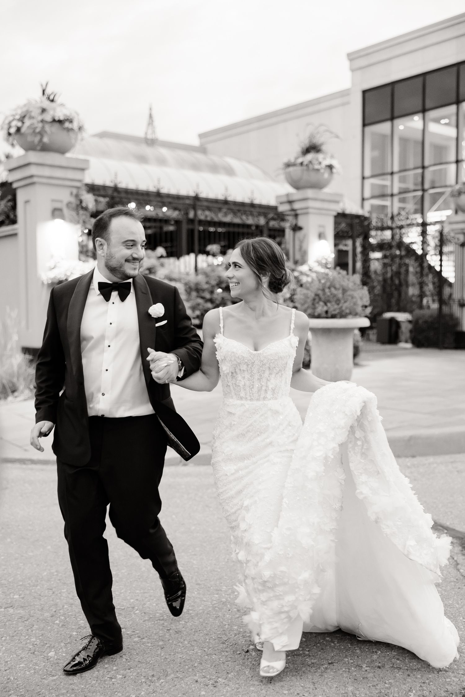 Black and white series showing a couple in wedding attire running and laughing together outside a shopping center.