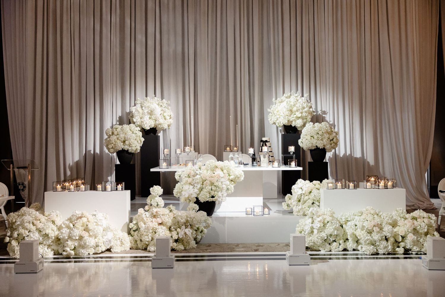 Elegant wedding reception banquet hall decorated with white floral centerpieces and soft curtain backdrops.