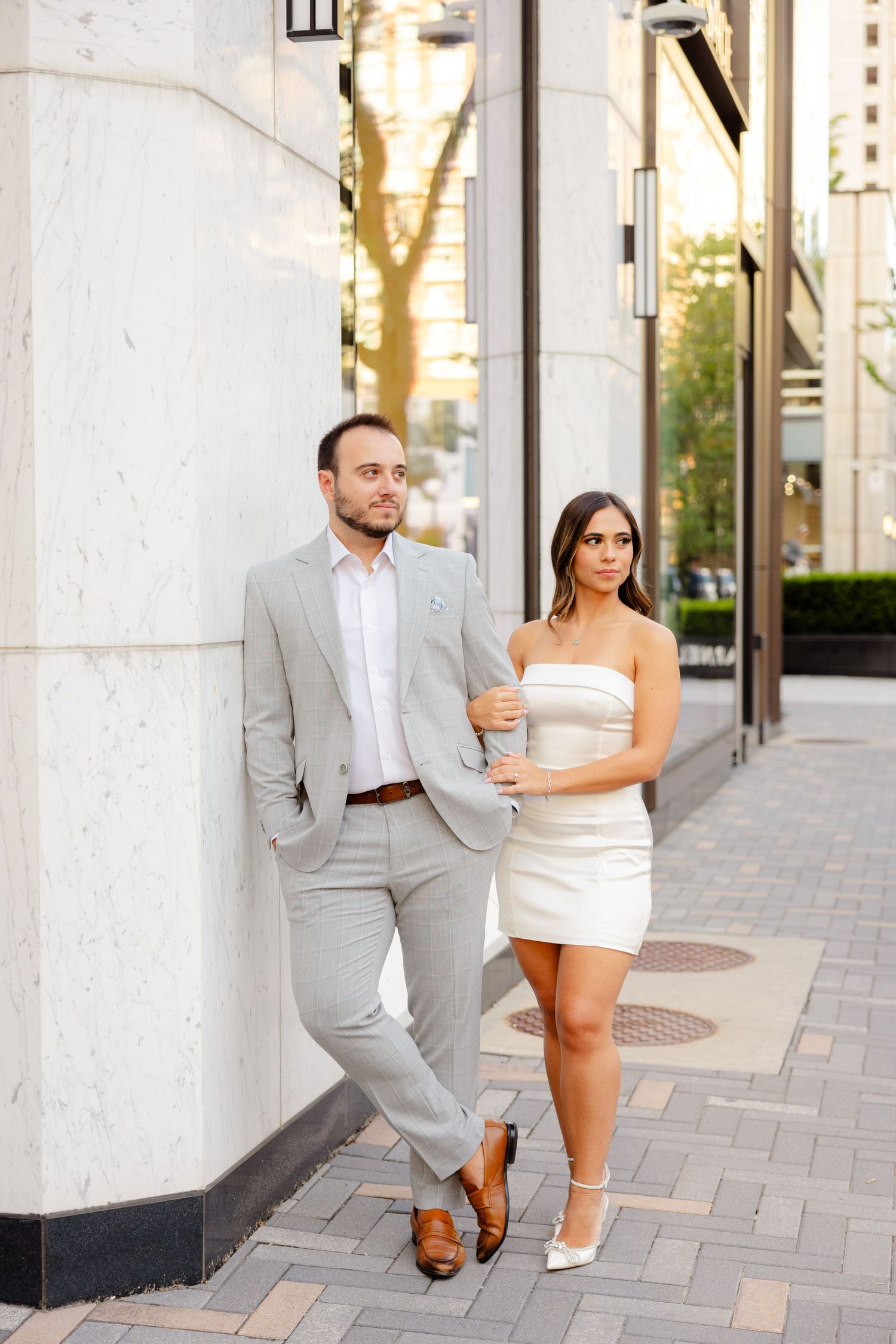 Well-dressed couple posing against white building exterior in an urban setting.