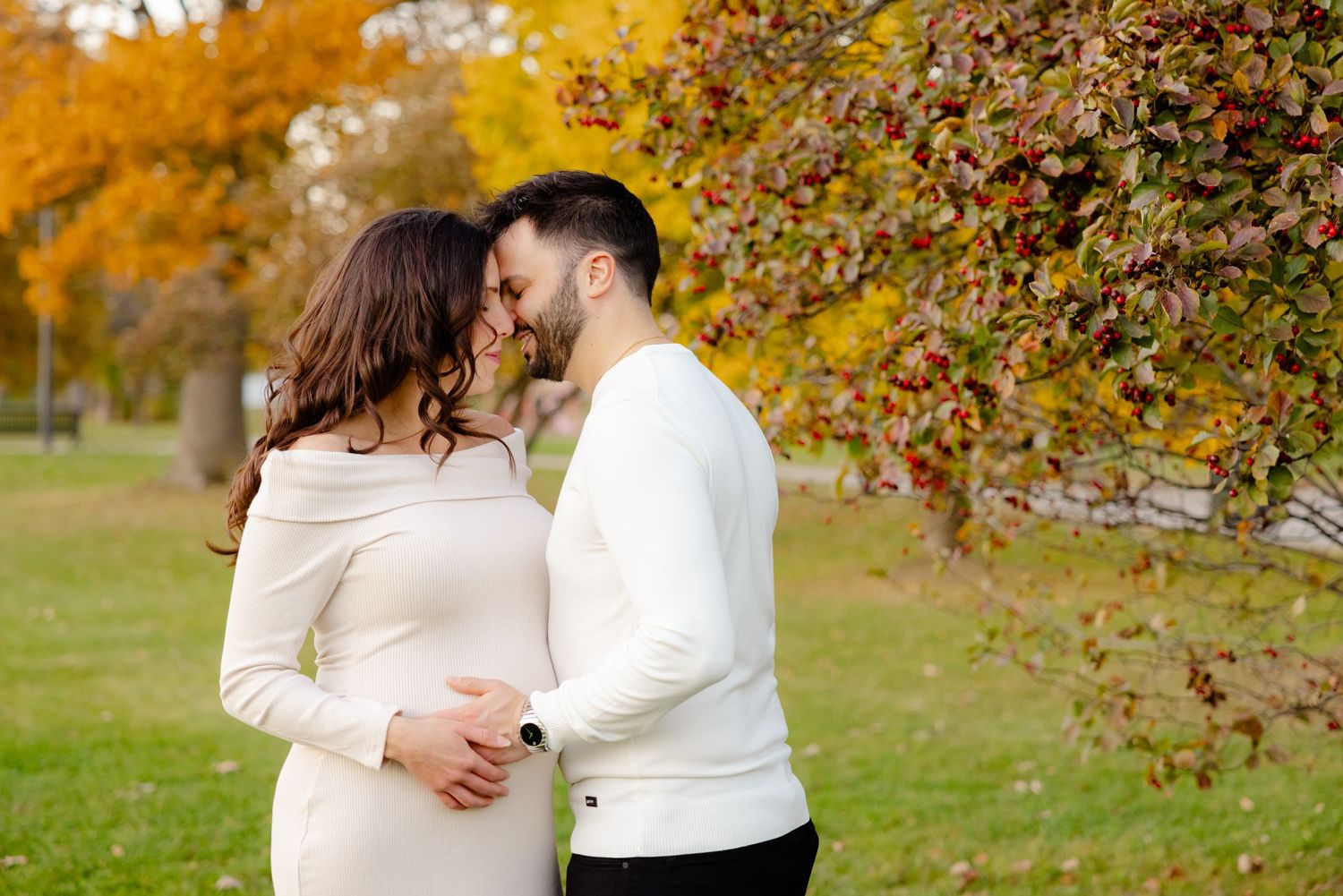 Couple embracing in autumn park with golden foliage and trees in background.