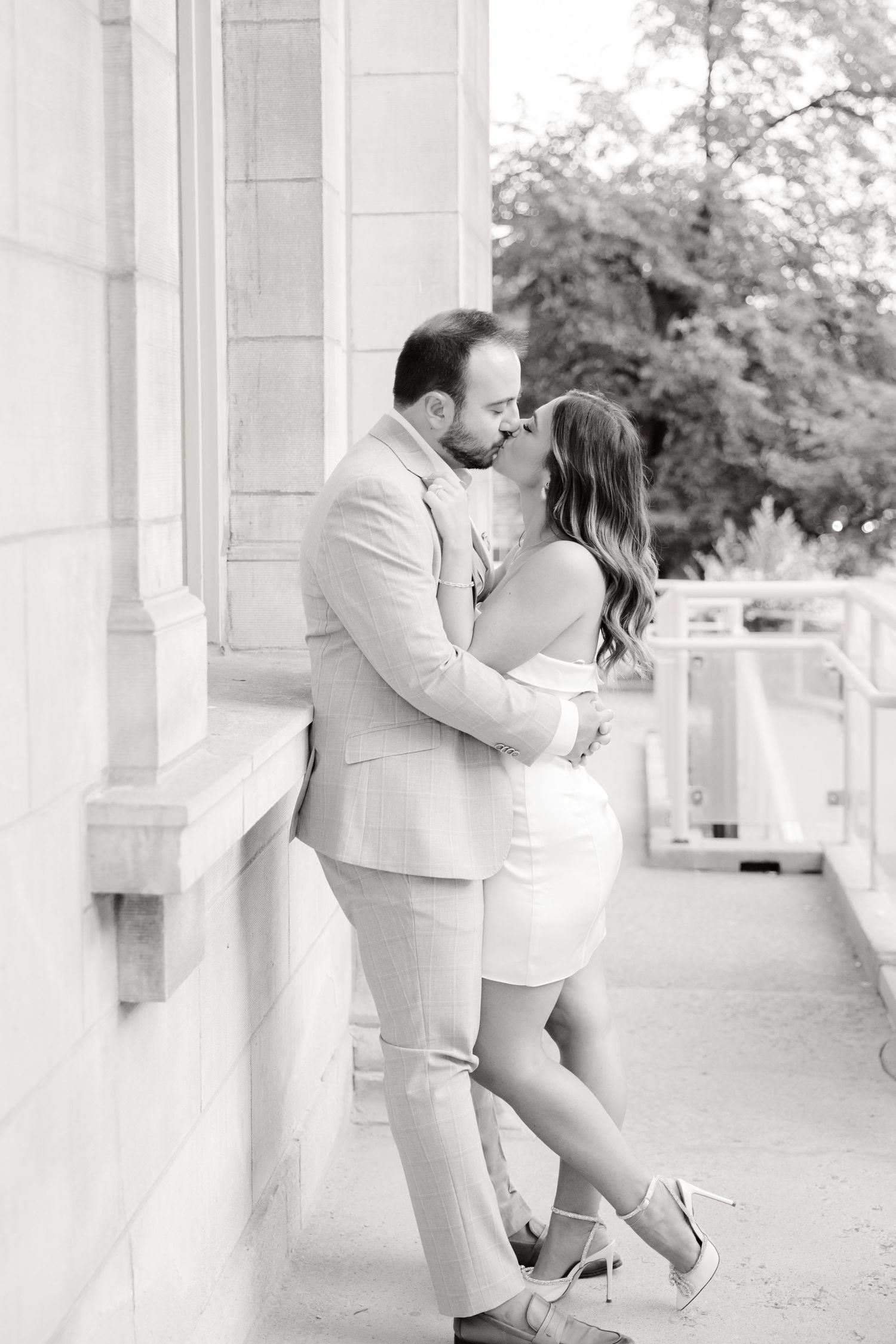A romantic couple shares an intimate moment on a classic columned porch wearing formal attire.