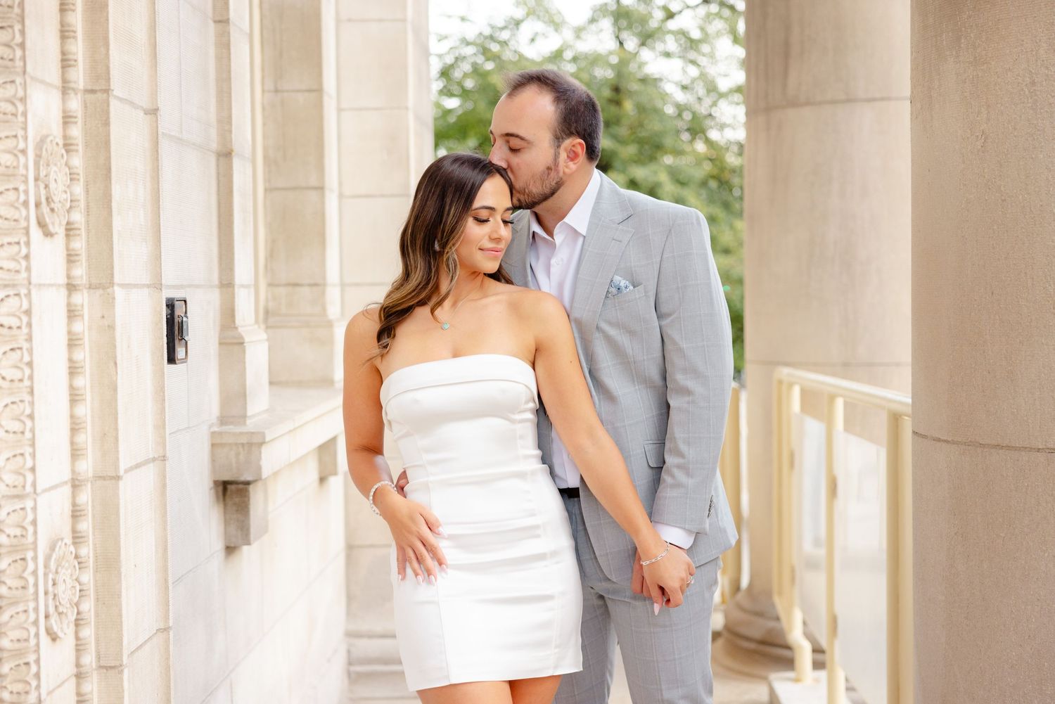 Couple shares an affectionate moment in an elegant columned walkway.
