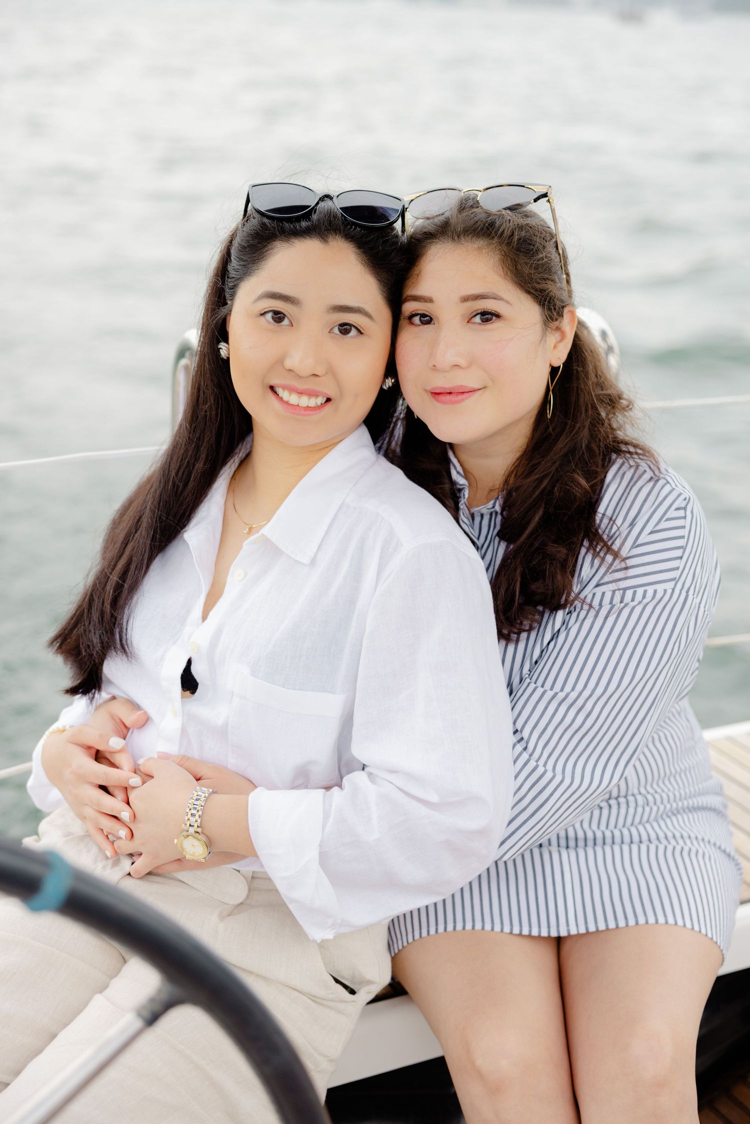 Two friends wearing white and striped shirts enjoy time together on a boat against a cloudy sky and water backdrop.