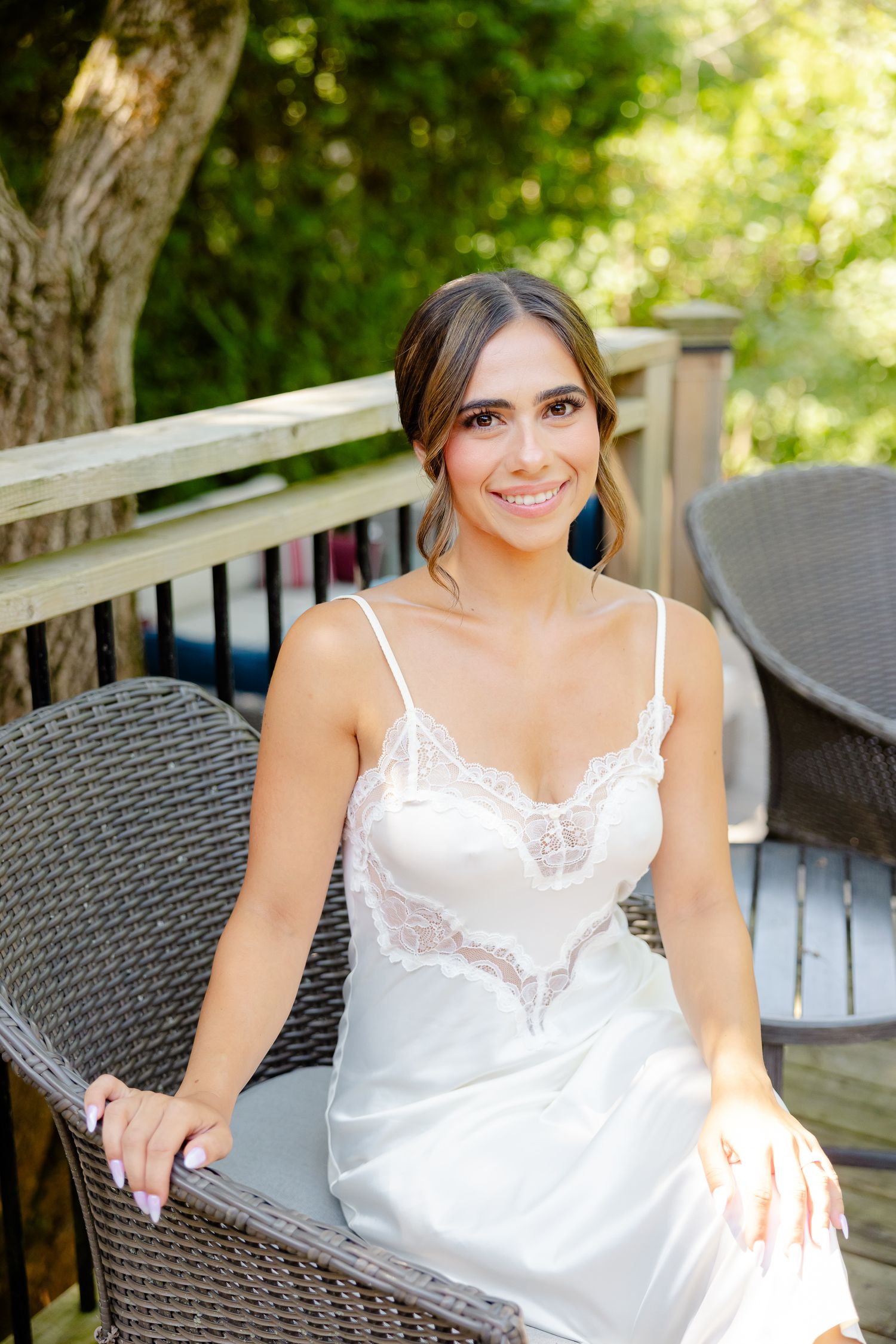 Someone in a delicate white lace-trimmed camisole sitting on outdoor wicker furniture on a wooden deck.