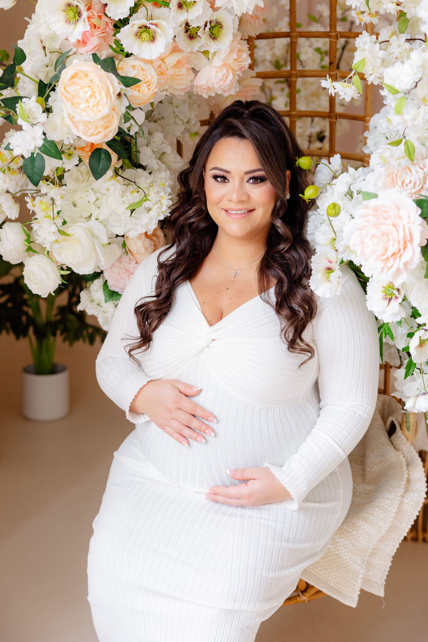 Beautiful maternity portrait in white dress with elegant floral backdrop of white and peach roses and greenery.