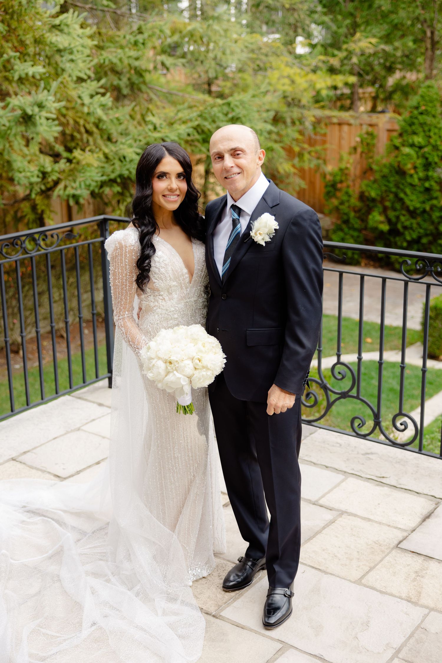 Elegant wedding portrait on a stone terrace with white floral bouquet and garden background.