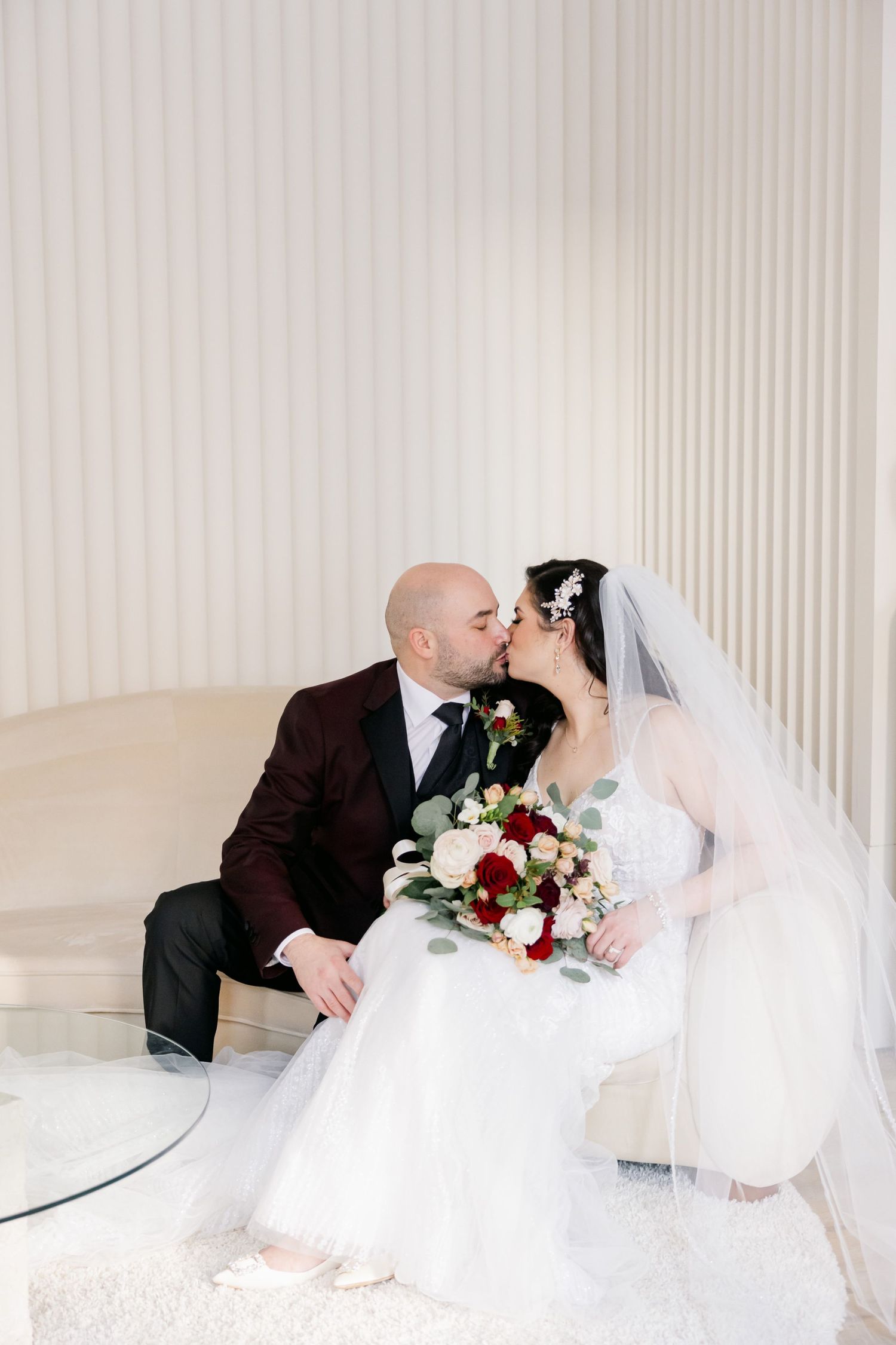 Romantic wedding photo of couple sharing a kiss while holding beautiful mixed flower bouquet.