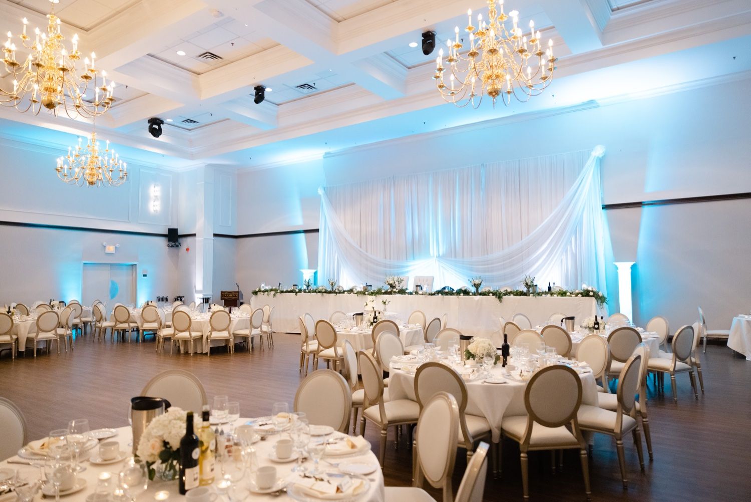 Elegant wedding reception ballroom with crystal chandeliers and blue uplighting.