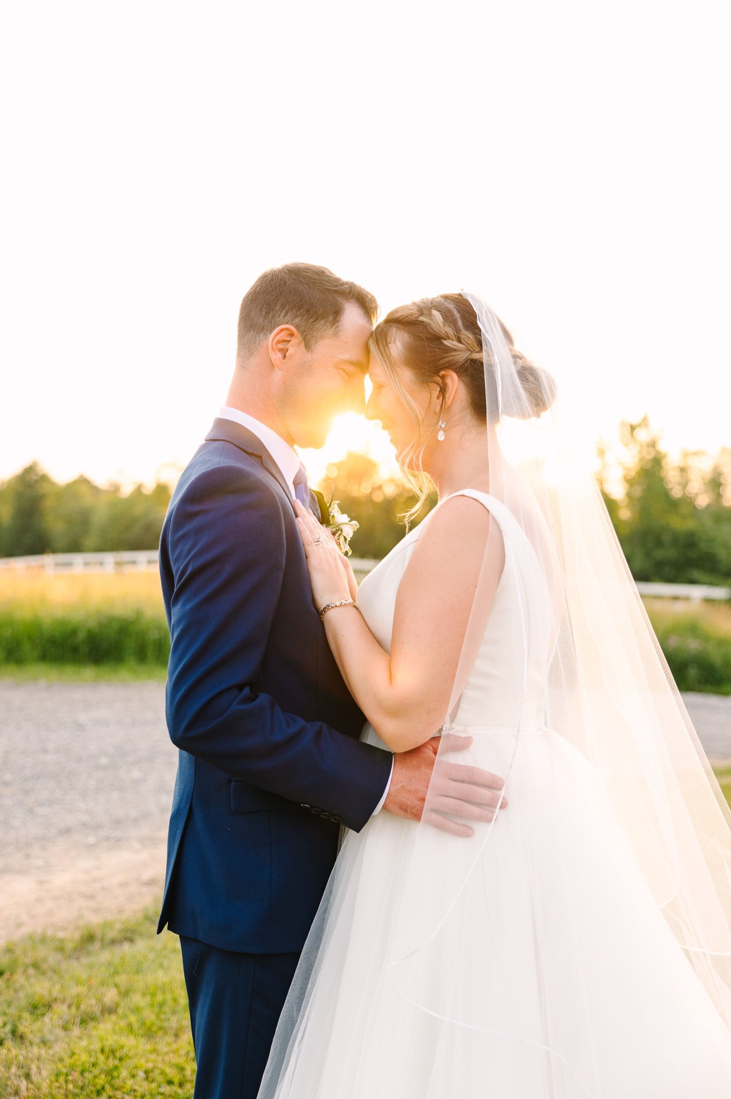 Romantic sunset portrait of couple embracing outdoors with golden light filtering through veil.