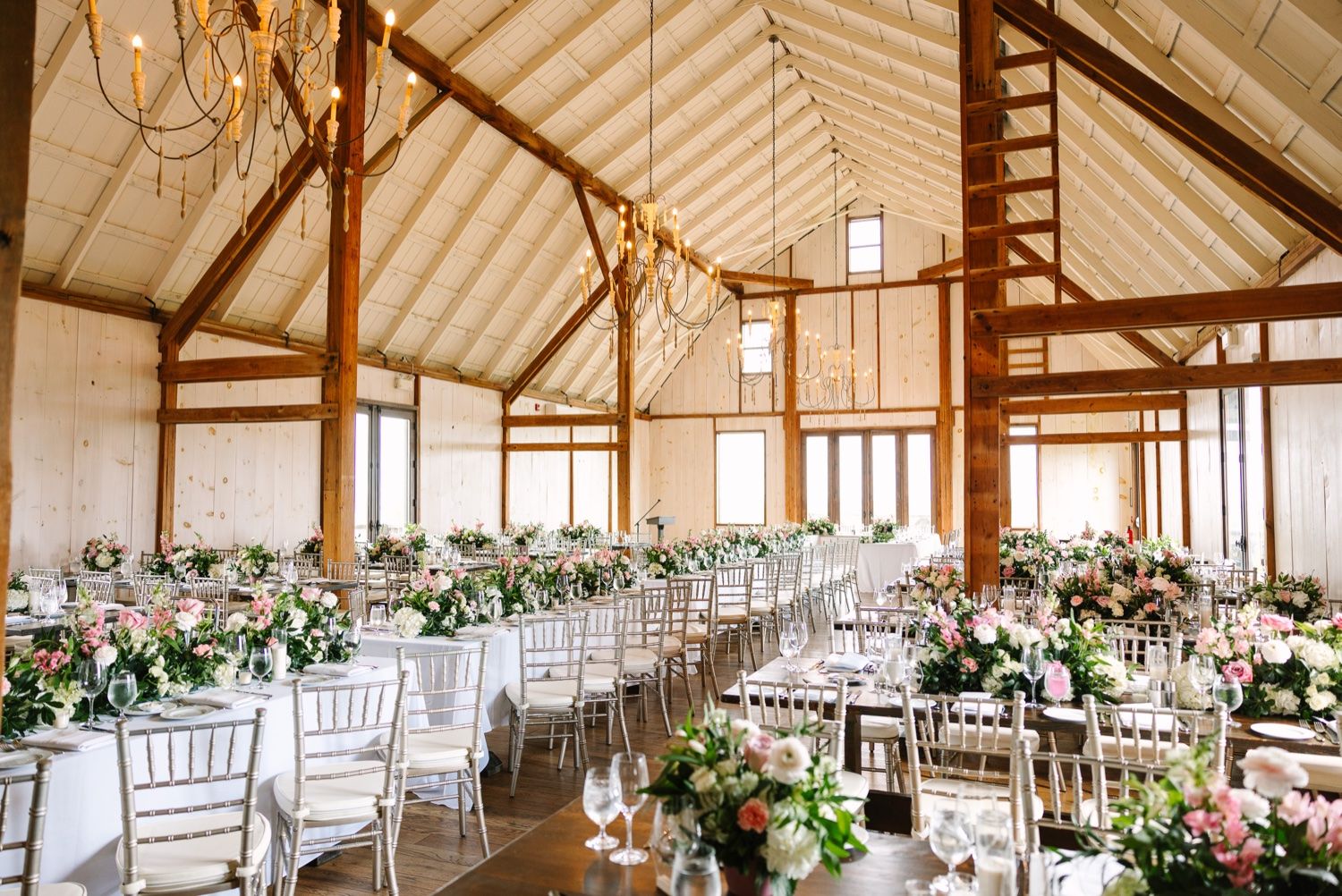 Elegant barn wedding reception venue decorated with floral arrangements and white chiavari chairs.
