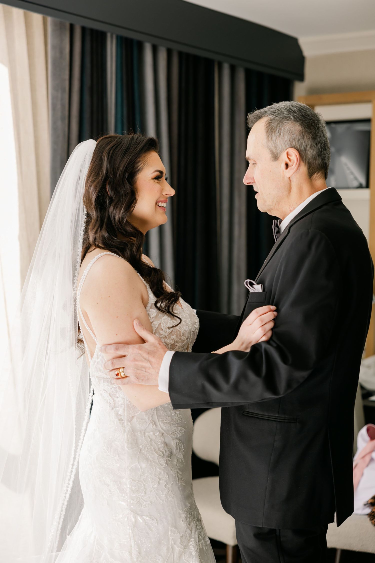 Intimate wedding moment captured in sunlit room with elegant curtains.