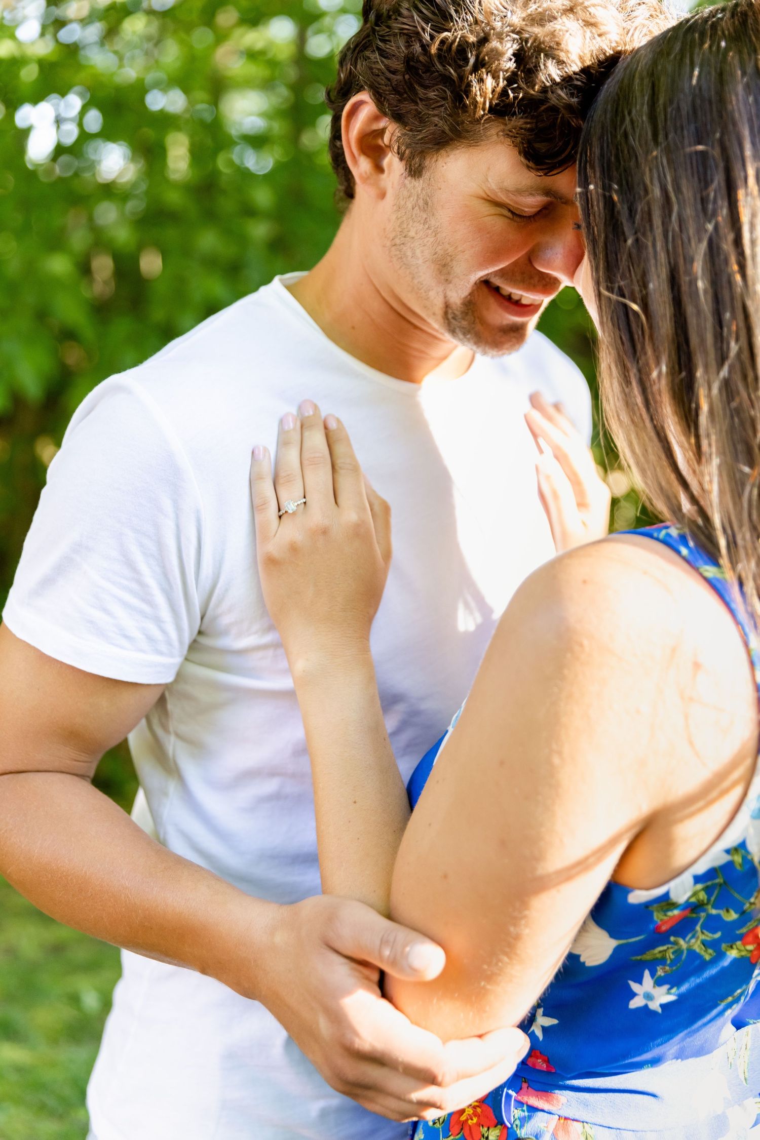 Close-up of tender moment between couple in white and blue outfits against forest backdrop.