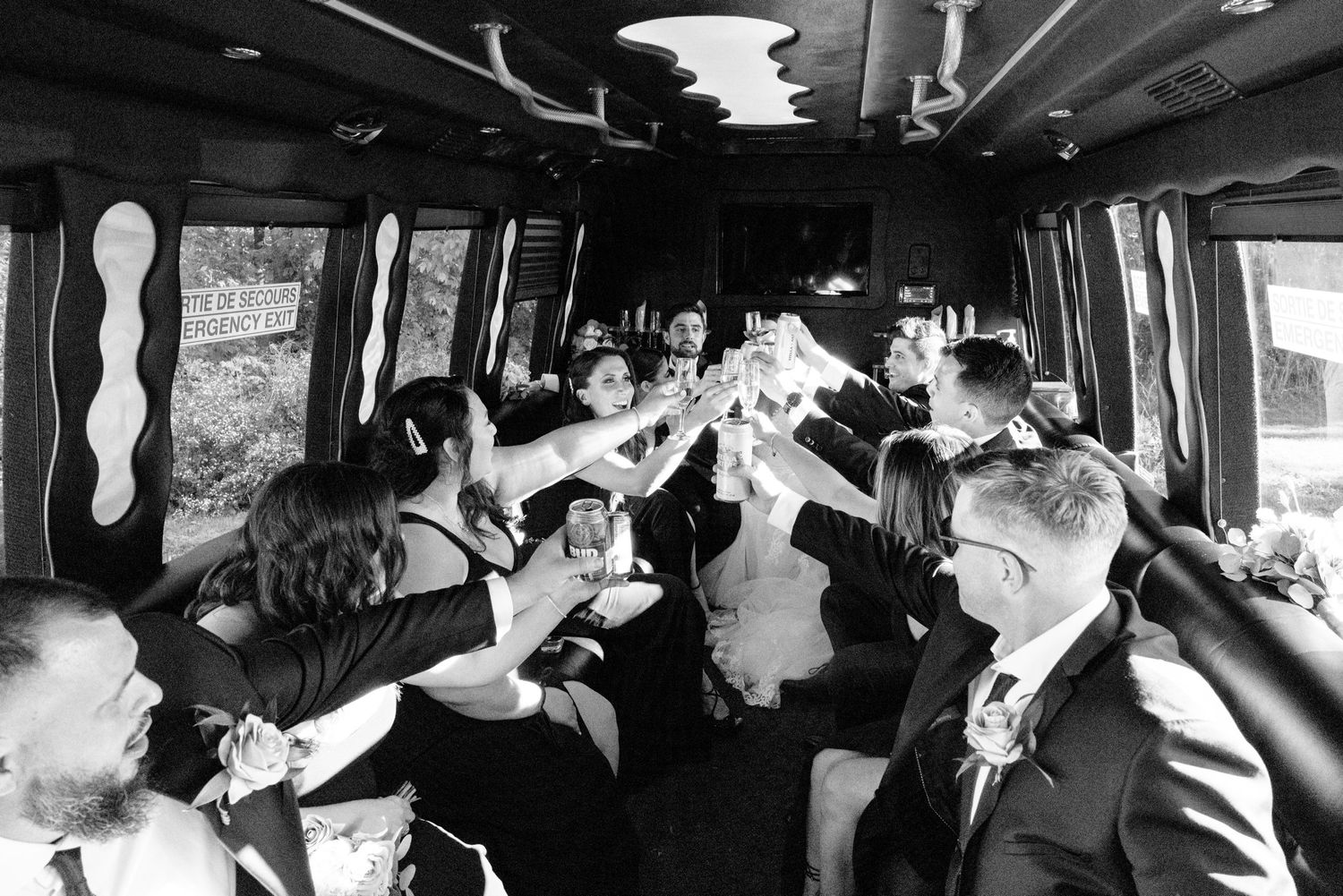 Black and white photo of wedding party celebrating with raised glasses in a party bus.