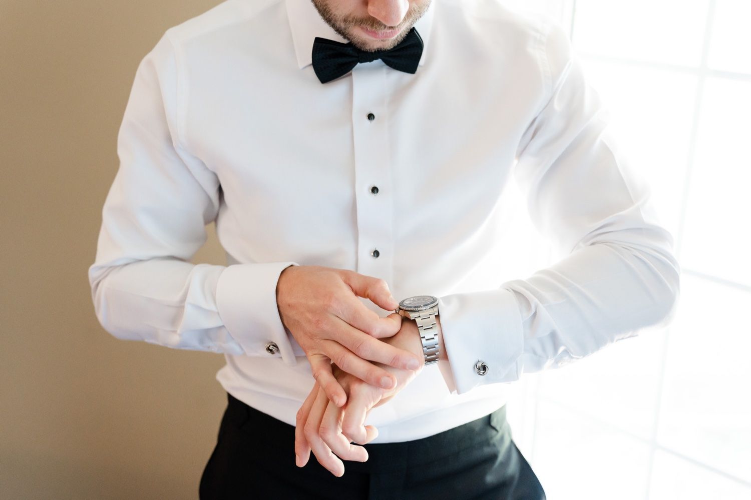 Groom checking his watch while wearing crisp white dress shirt and bow tie.
