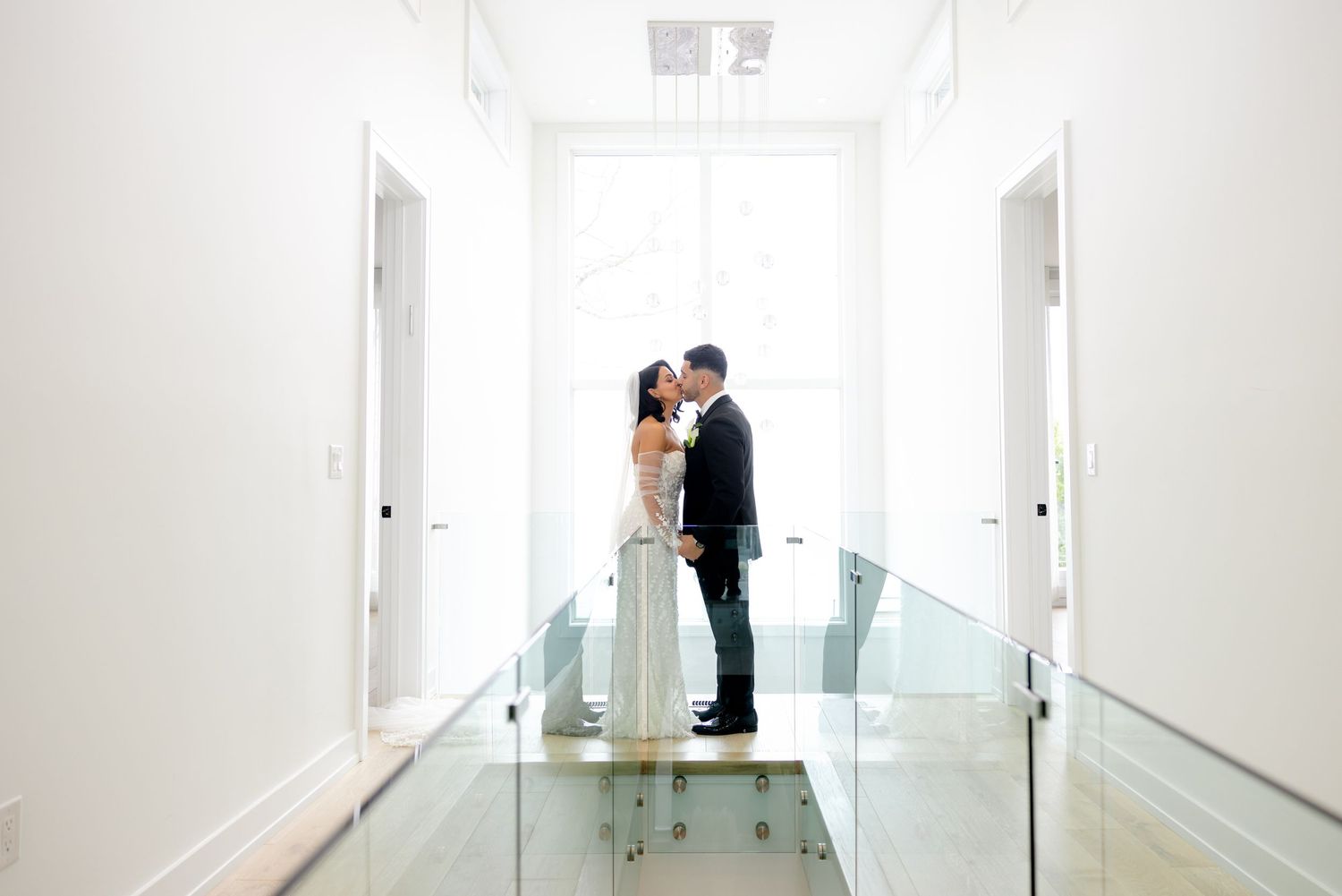 Two individuals share an intimate moment in a bright white hallway with glass railings.