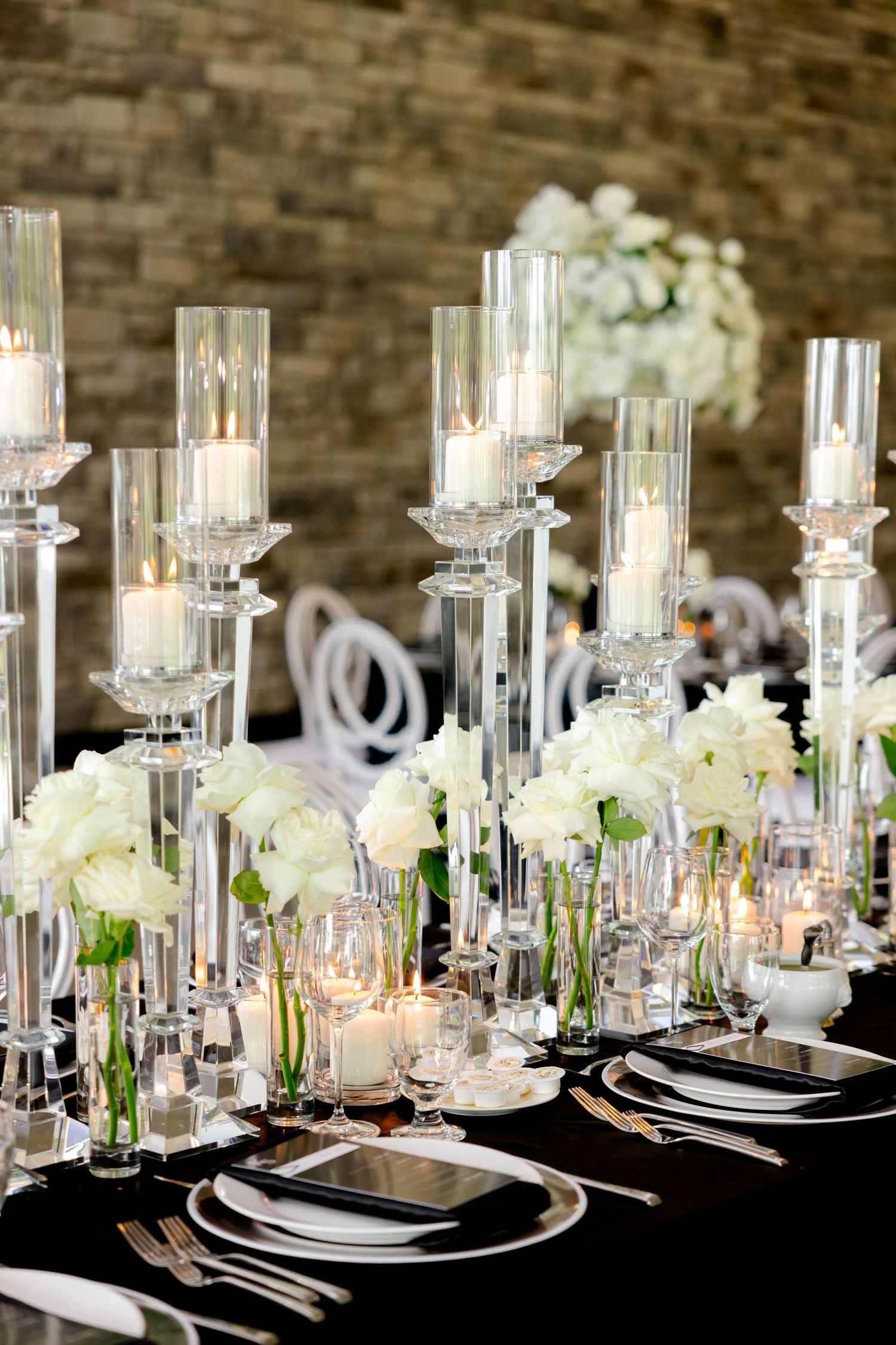 Elegant black and white wedding table settings with tall glass candleholders and white floral arrangements.
