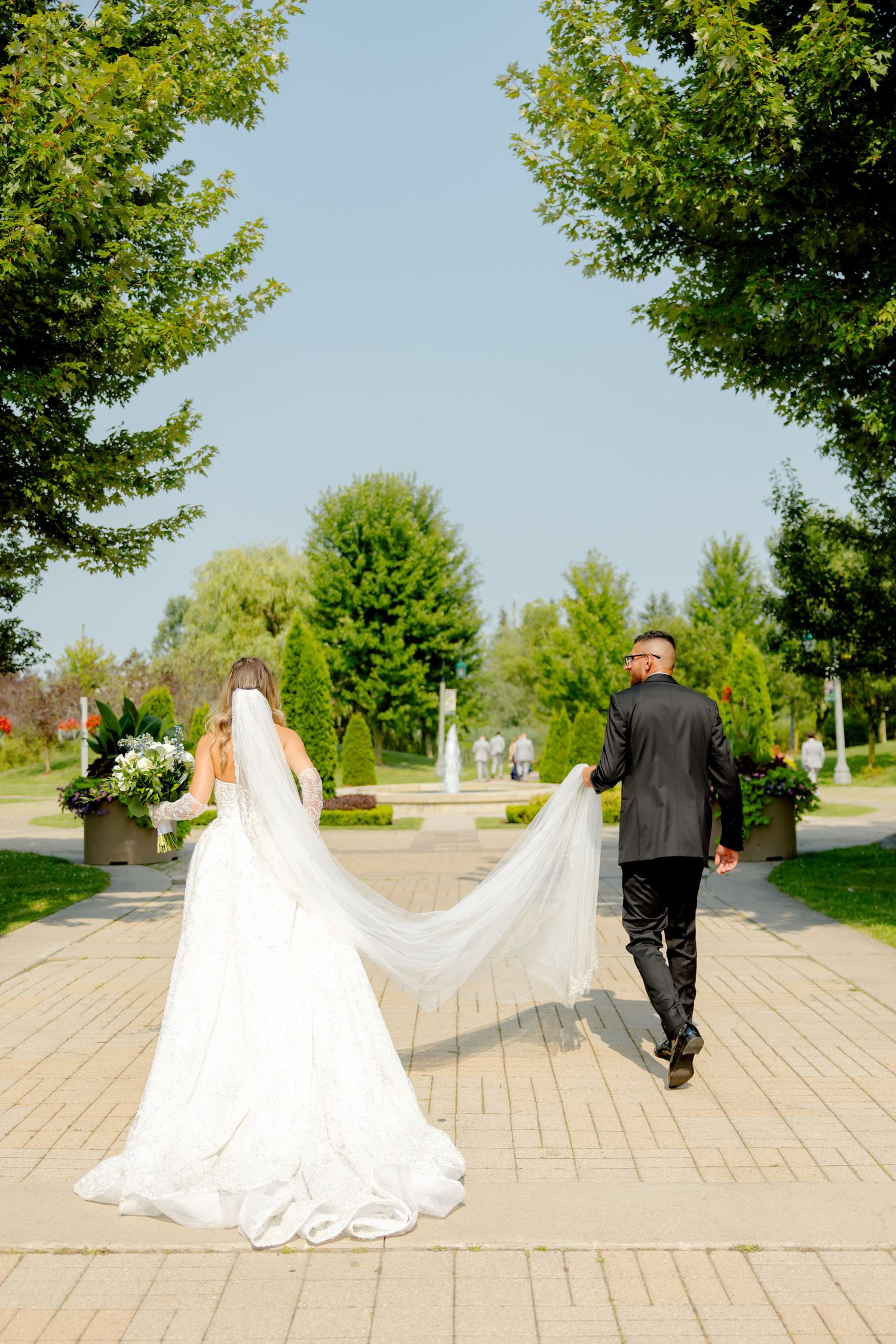 Newlyweds walking away on brick path with flowing veil trailing behind.