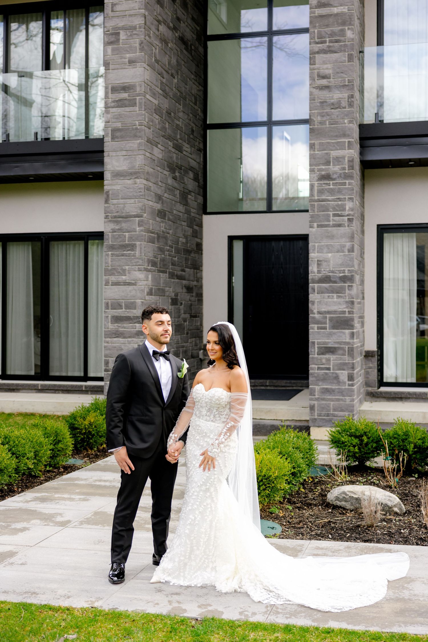 An elegant couple poses for their wedding photos in front of a modern stone and glass building.
