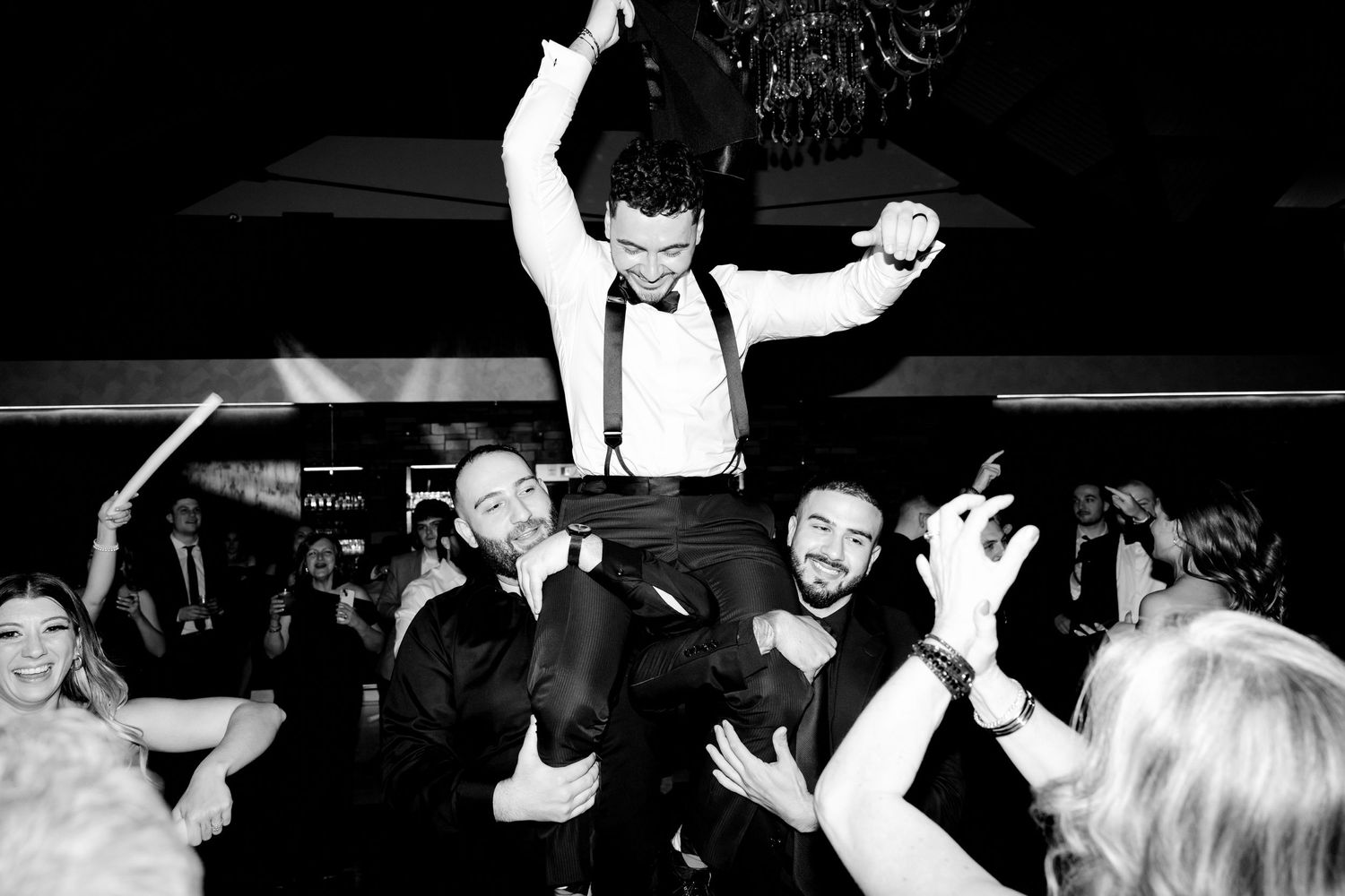 Wedding celebration with groom being lifted up by guests during reception party in black and white photography.