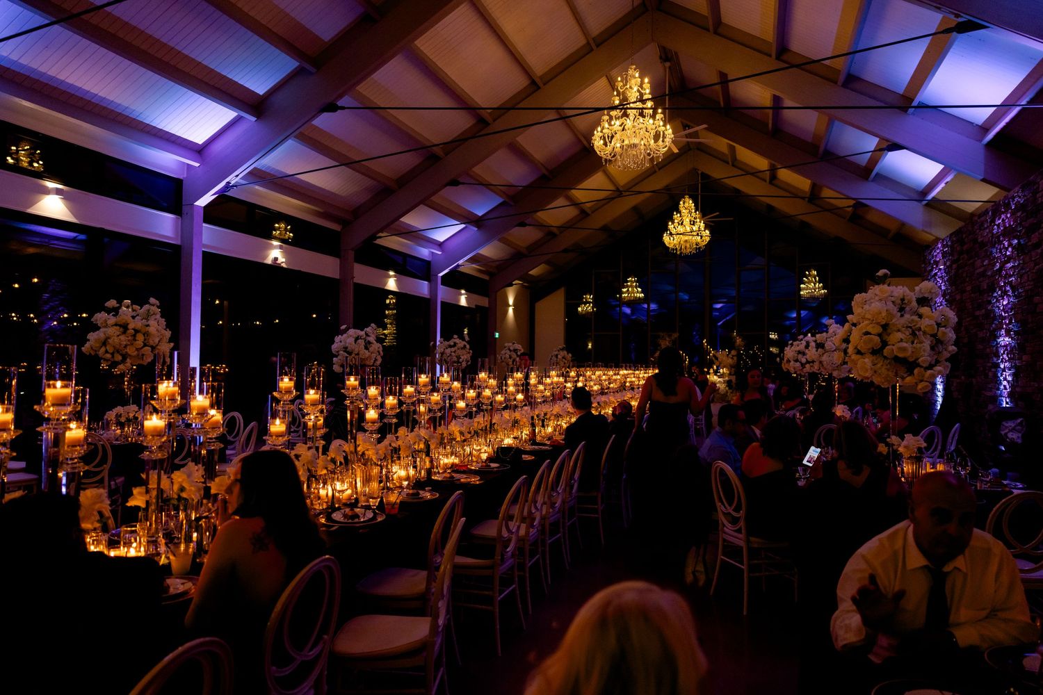 Wedding reception venue lit with purple uplighting and elegant chandeliers creating romantic atmosphere.