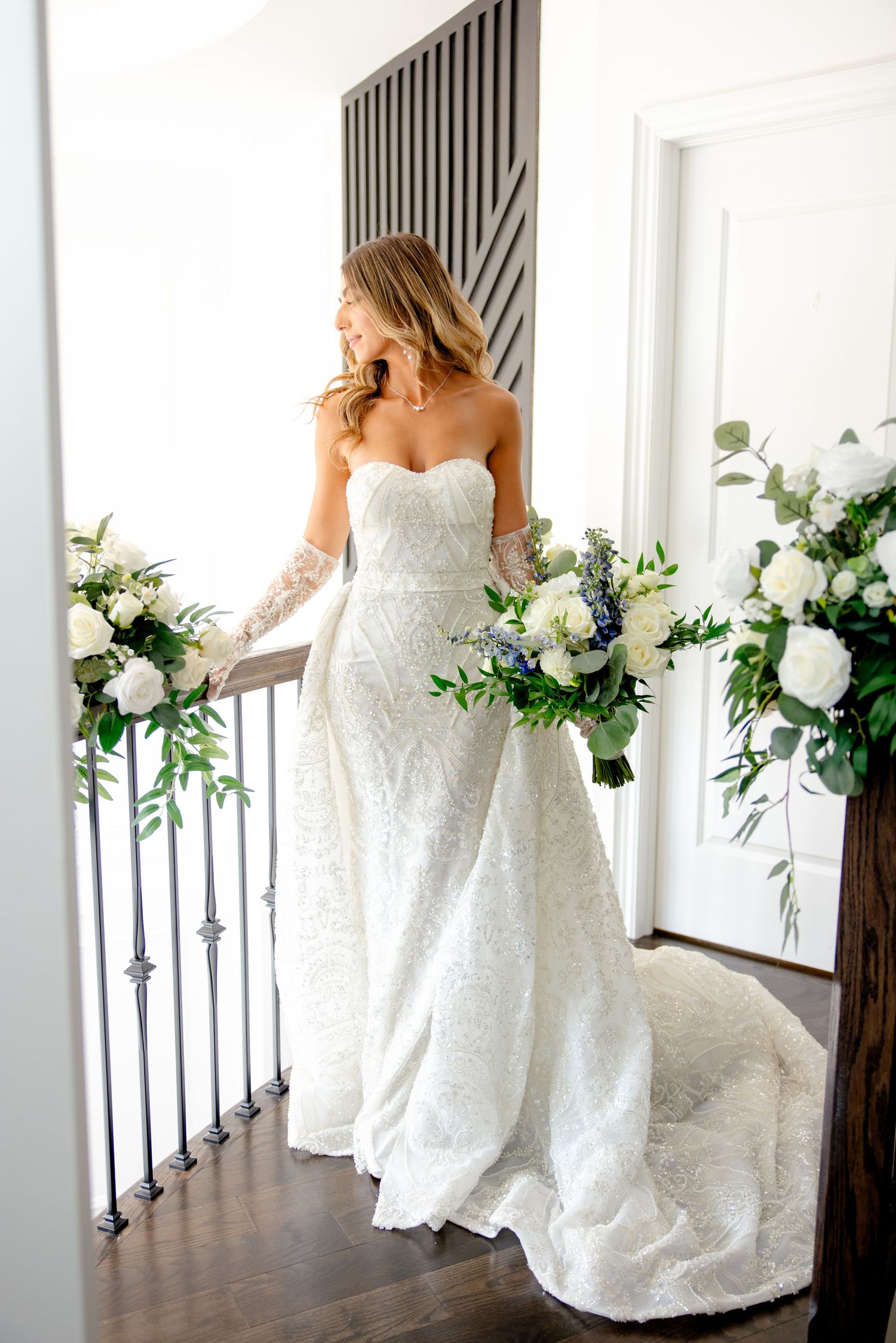 Elegant wedding gown with lace details and train photographed in a modern interior with floral decorations.