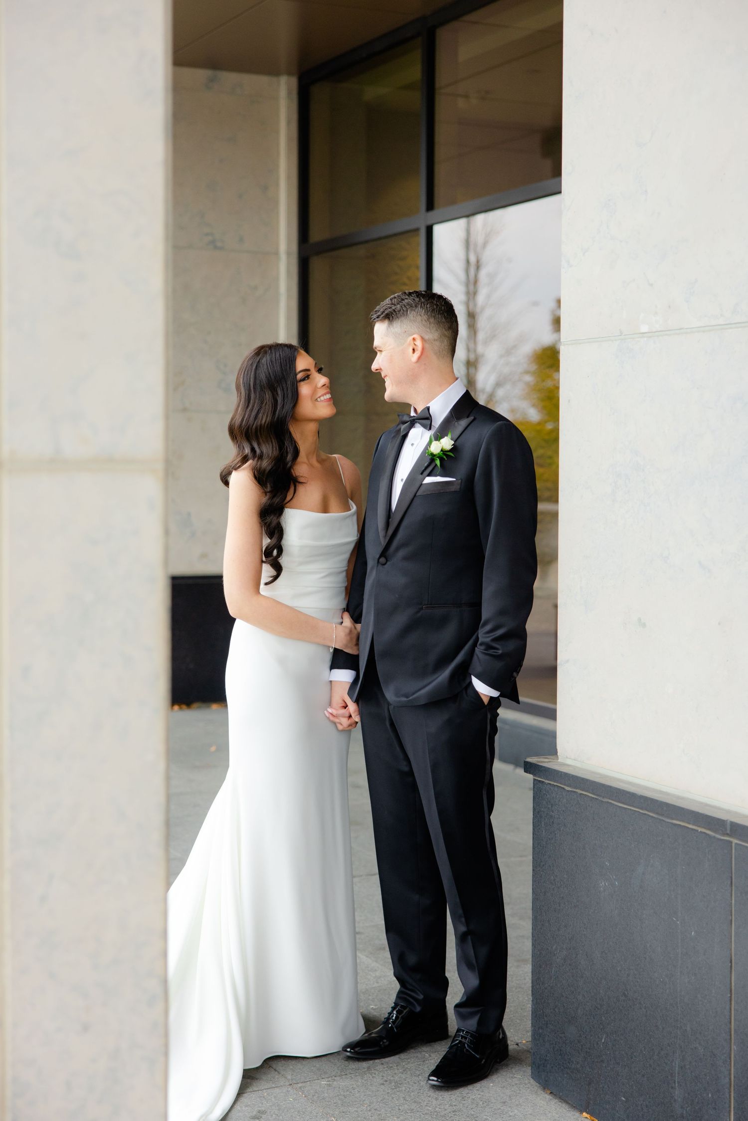A wedding couple shares an intimate moment in an elegant covered walkway with glass windows.