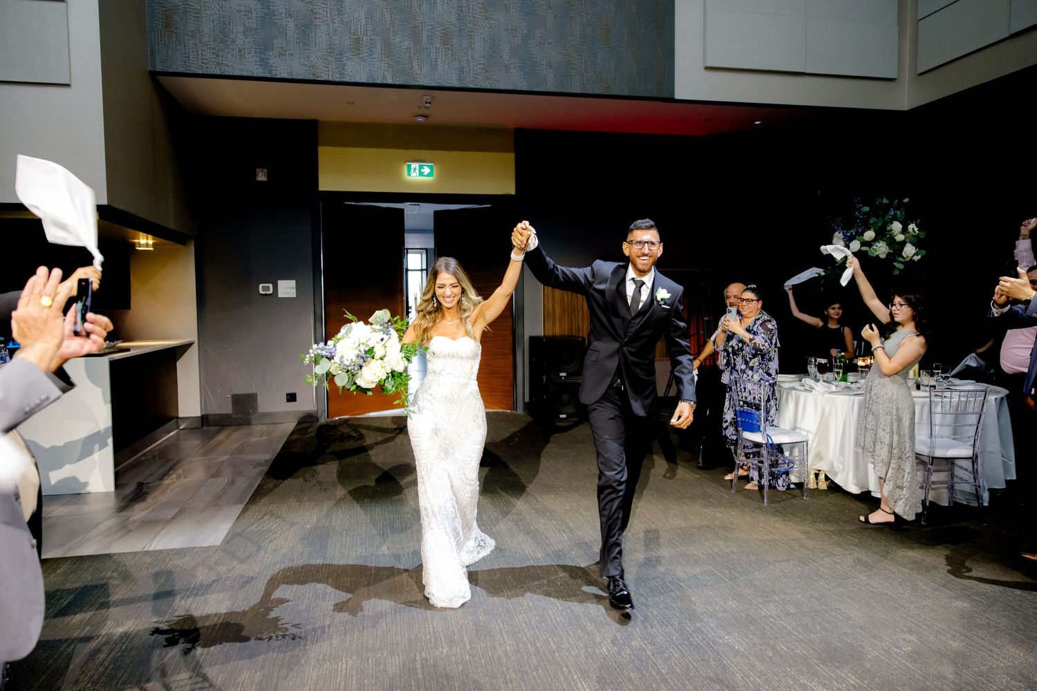 Bride and groom make their grand entrance into the reception with raised arms in celebration.