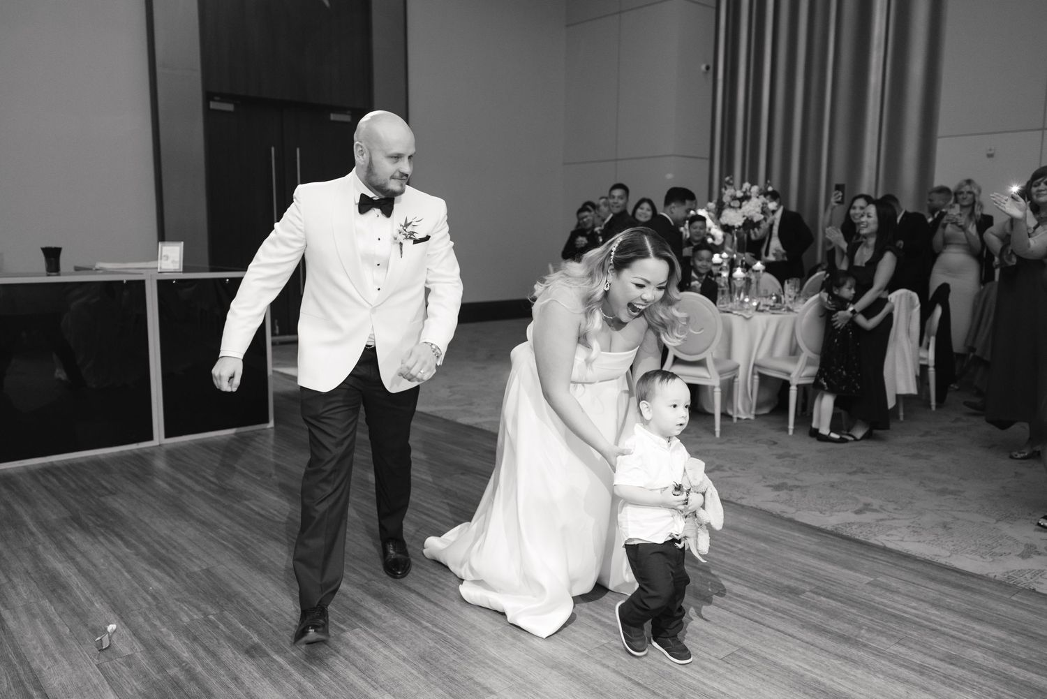 Black and white photo of wedding guests dancing together on a hardwood floor during a reception.