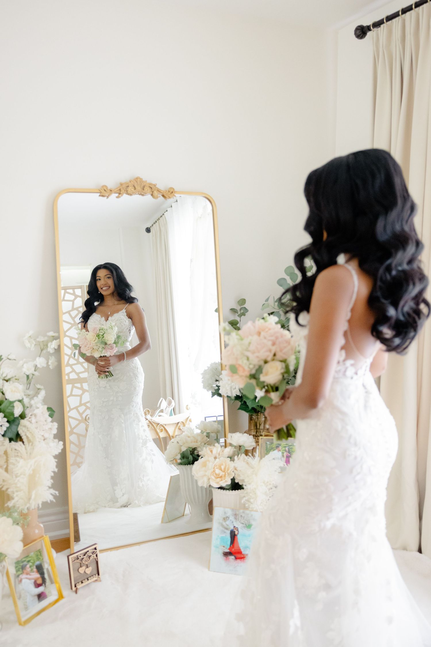 A stunning bridal portrait showing an elegant white lace gown reflected in an ornate gold-framed mirror with floral decorations.