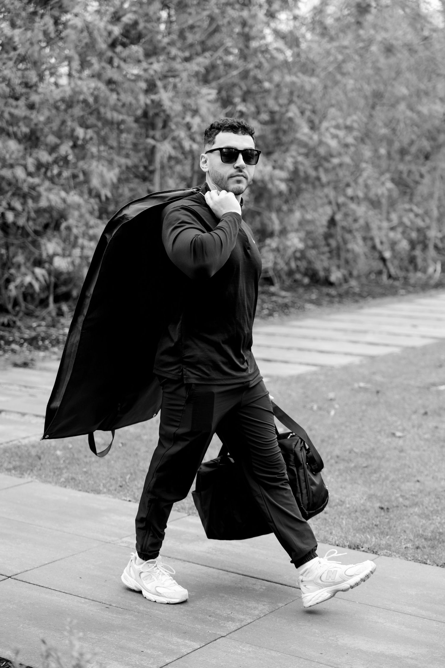 Black and white photo of person in athletic wear carrying garment bag.